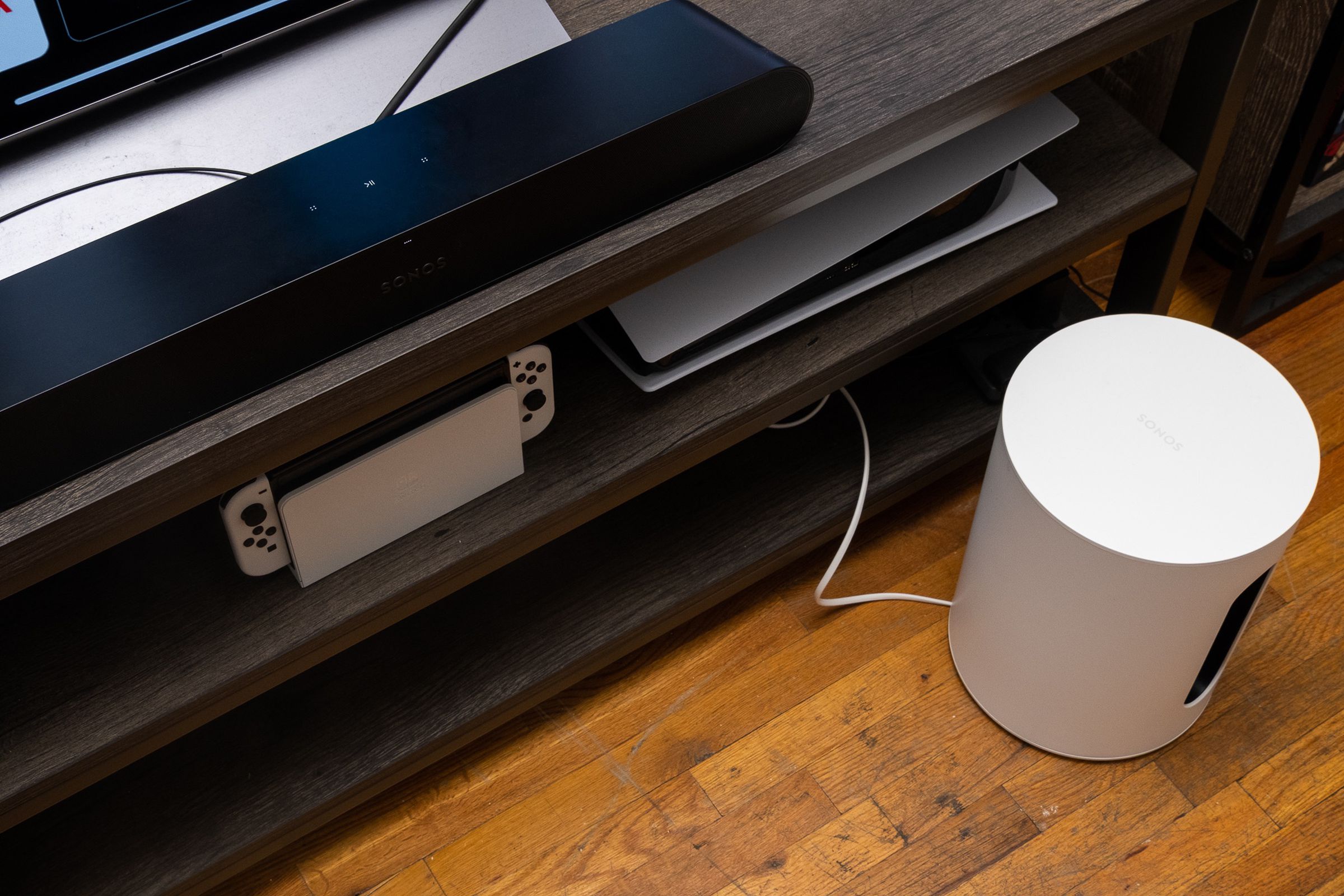 An image of the Sonos Sub Mini subwoofer on the floor near a TV stand with a Sonos Ray soundbar.