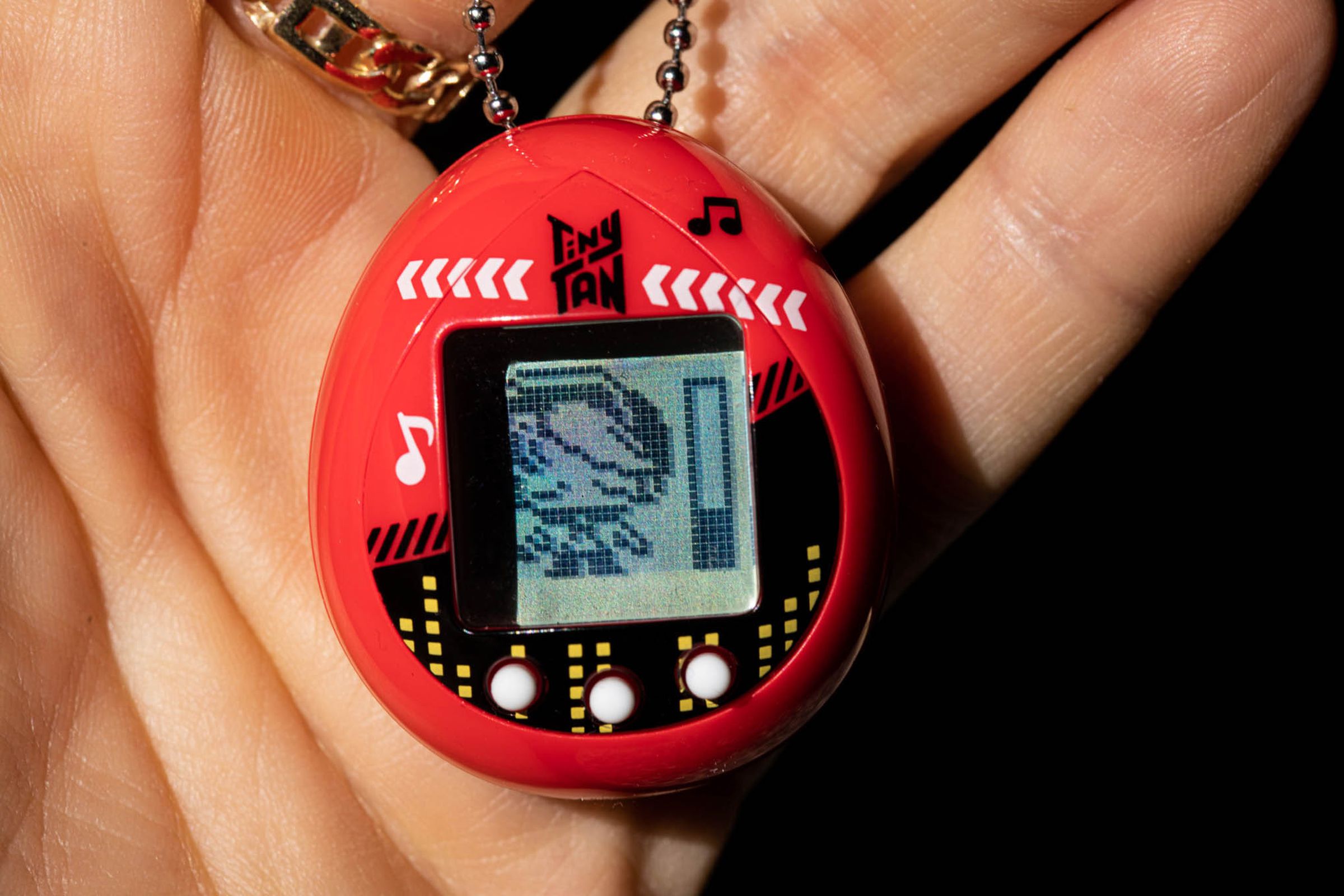 A user holds the TinyTan Tamagotchi. The screen displays a character sleeping with a stamina bar a quarter full beside it.