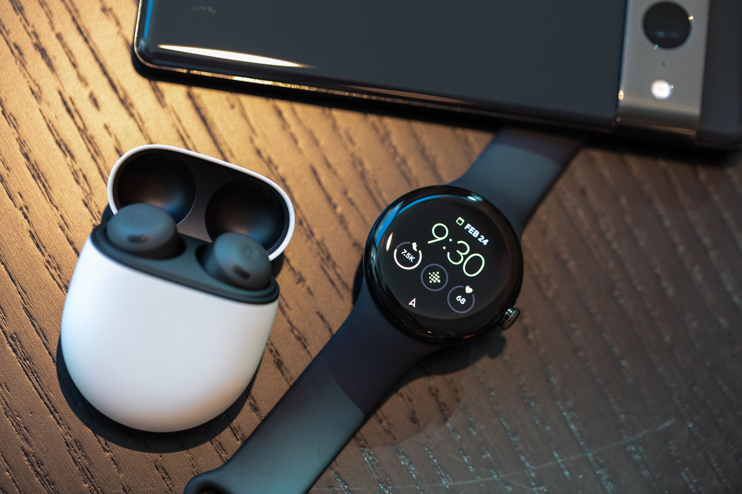 The Pixel Watch next to the Pixel Buds in their case and a Pixel 7 phone.