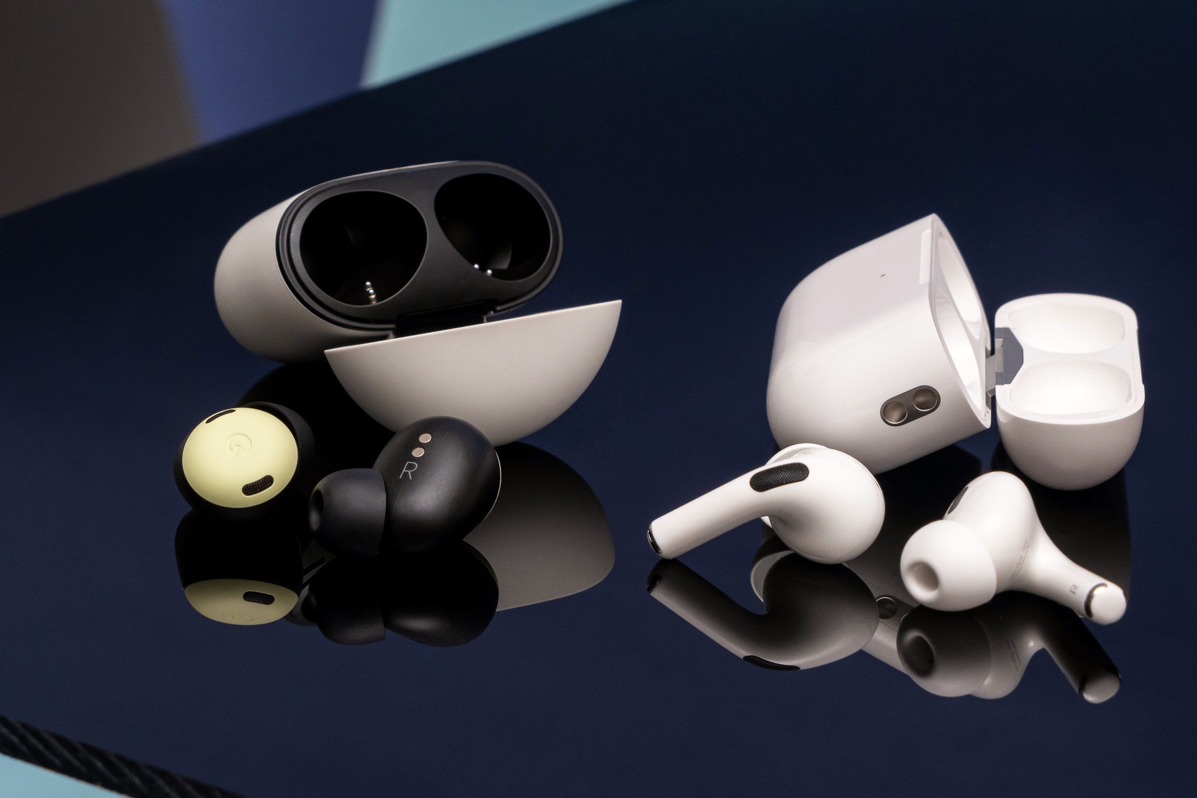An image of Google’s Pixel Buds Pro and Apple’s second-gen AirPods Pro next to each other on a table.