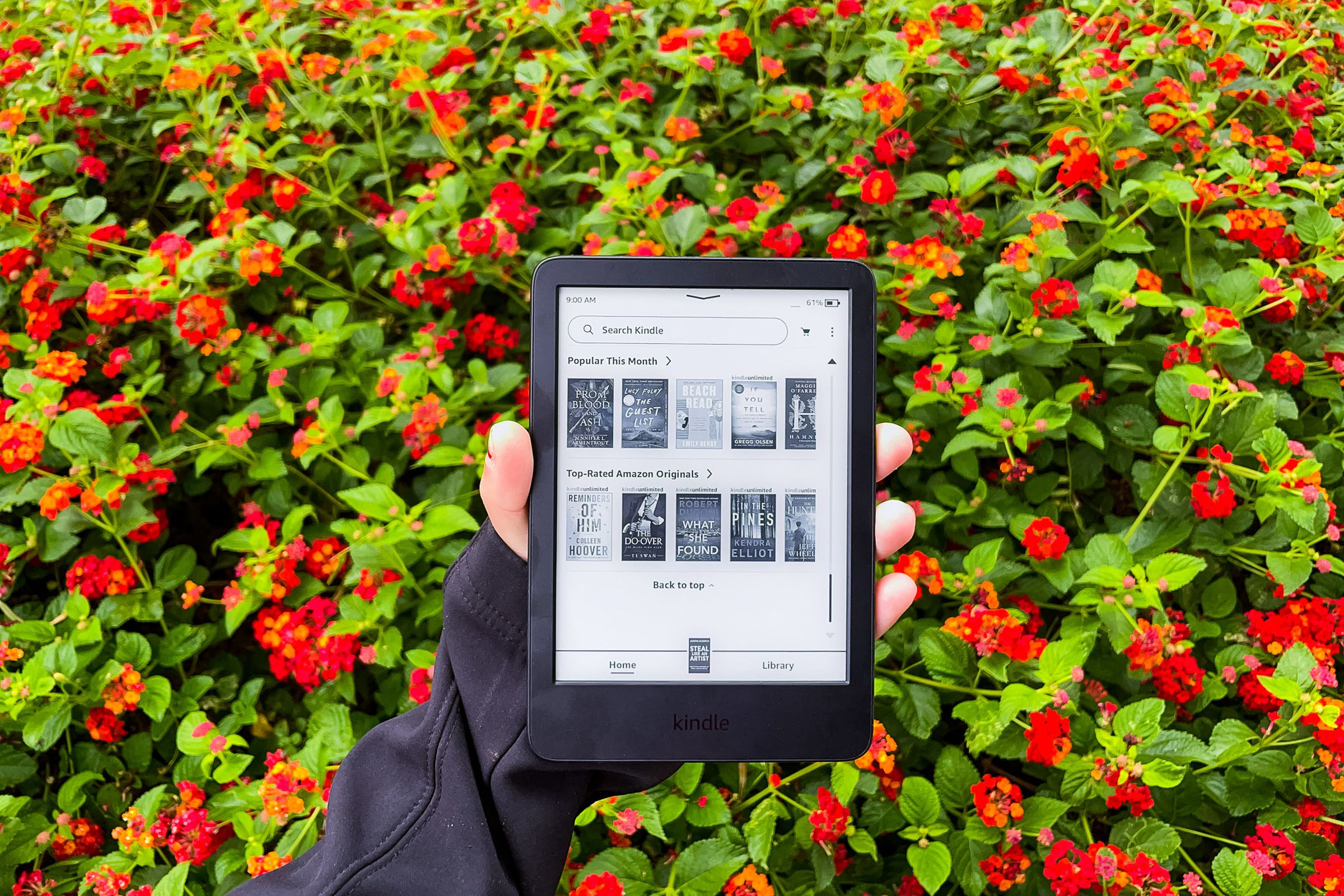 A hand holding the Kindle and displaying the main menu of the device.