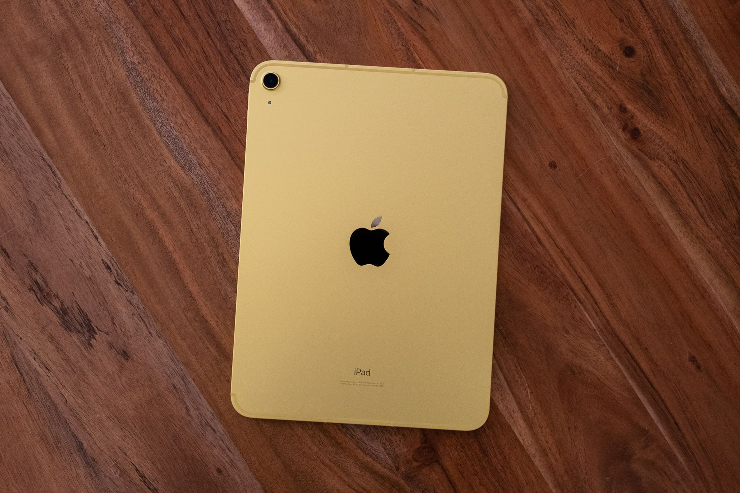 A yellow 10th gen iPad face down on a wooden table, seen from above.