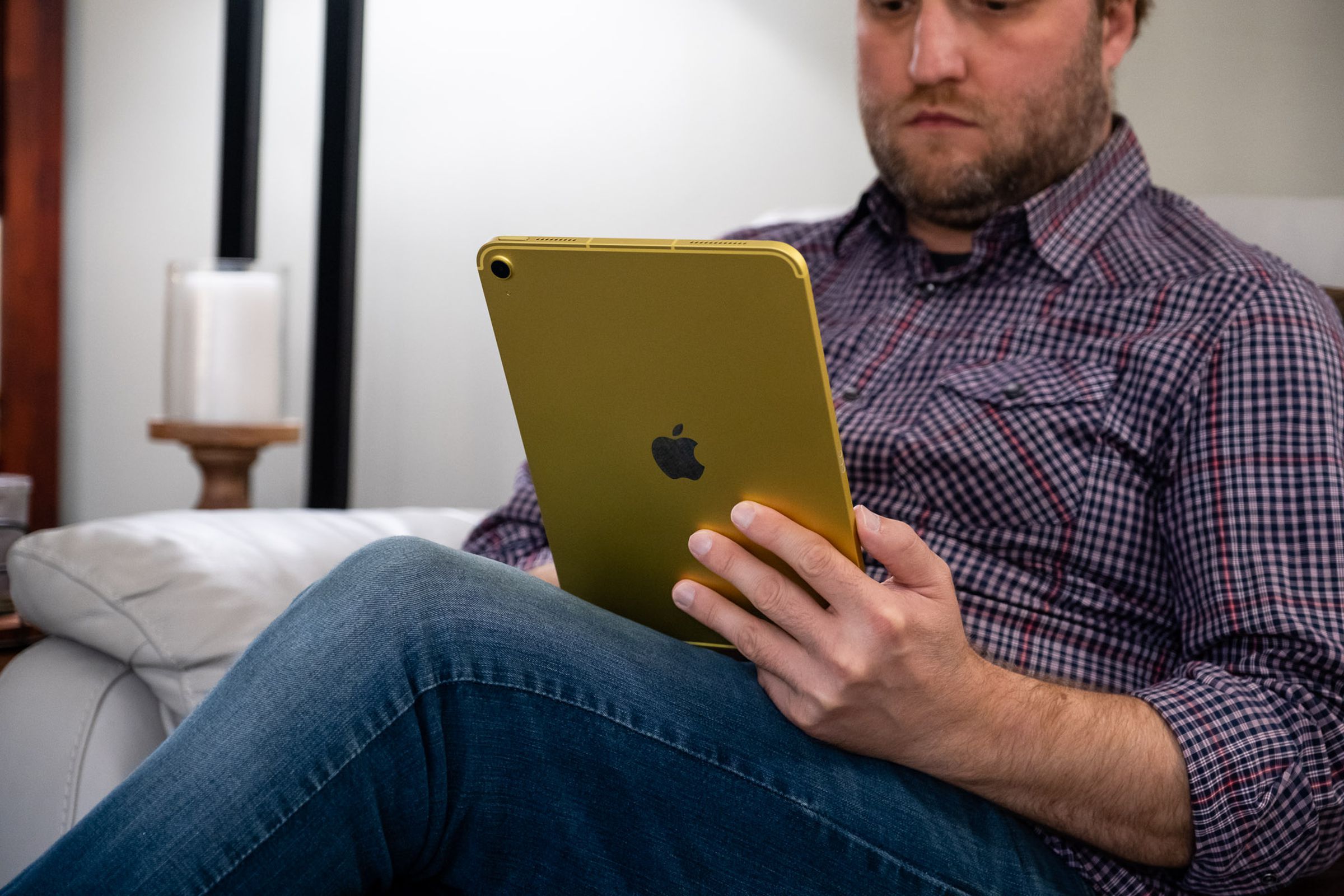 An adult man holding a yellow Apple iPad 10th gen in his left hand and looking at the screen.