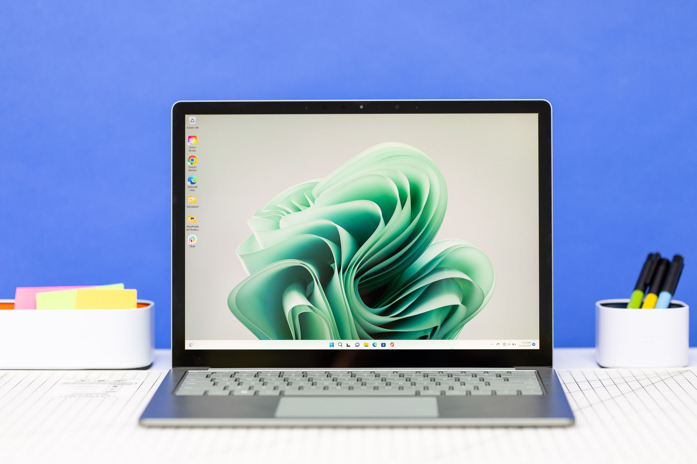 The Microsoft Surface Laptop 5 open on an office table. The screen displays a green ribbon.