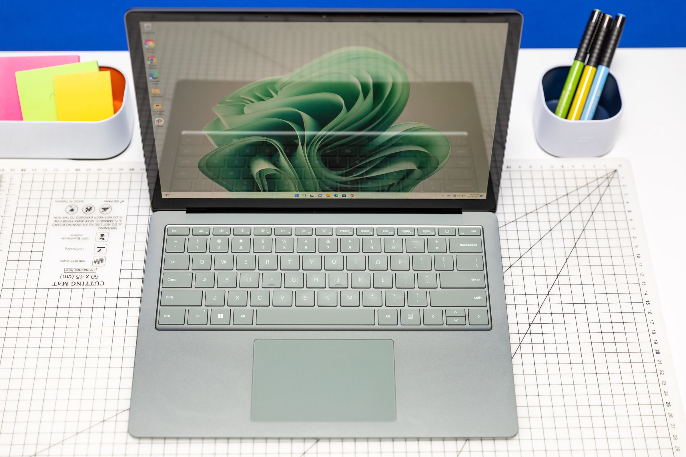 Yüzey Dizüstü Bilgisayarı 5 yukarıdan görülüyor, açık, bir masanın üzerinde Post-it ve kalemlerle. Ekranda yeşil bir şerit görüntülenir.