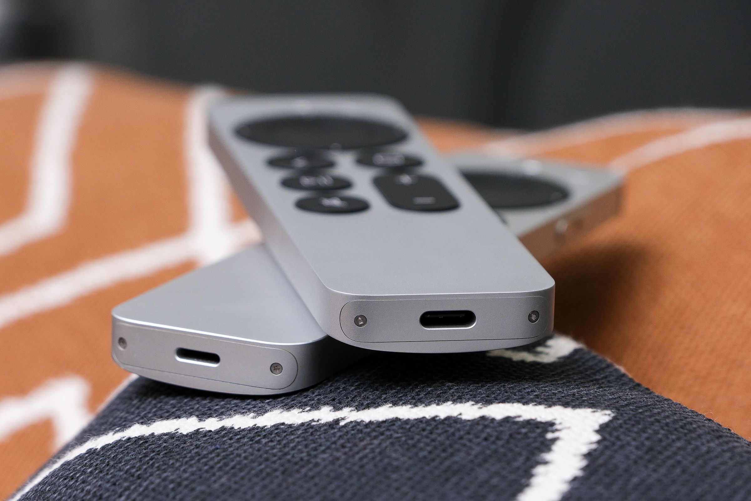 A photo of two Siri Remotes for the Apple TV. One has a Lightning port and the other has a USB-C port.