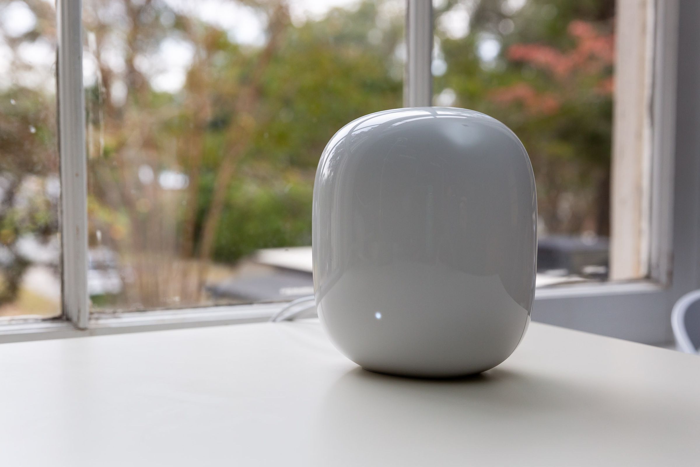 White Google Nest Wifi Pro router on a white table in front of a window.