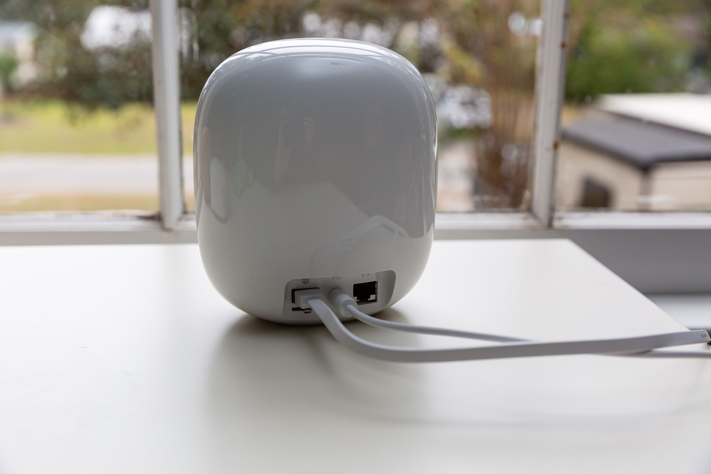 The back of a Nest Wifi Pro router on a table next to a window.