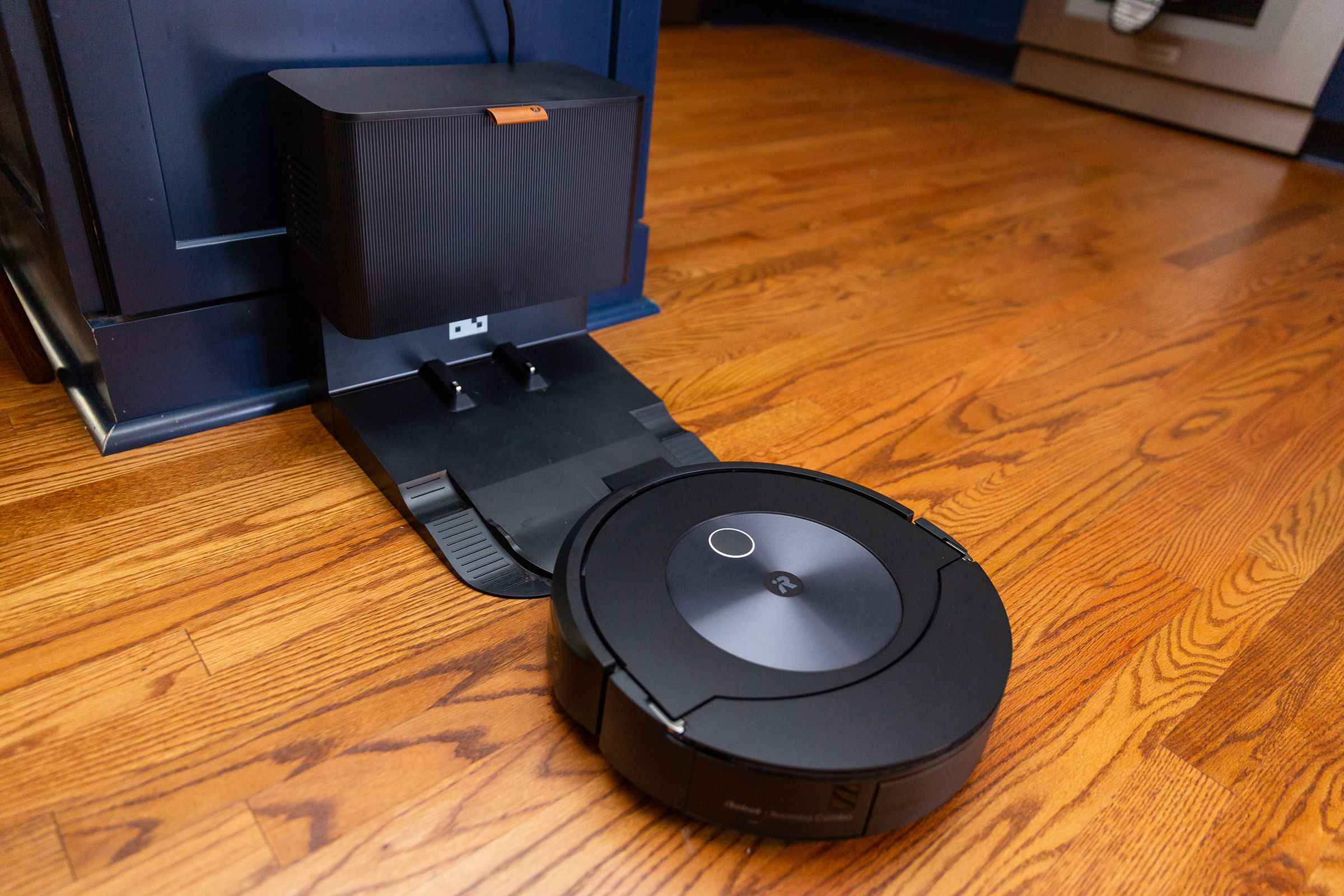 Foto del Roomba Combo J7 acercándose a su base vacía de forma automática.  La base es del tamaño de un pequeño bote de basura de cocina.