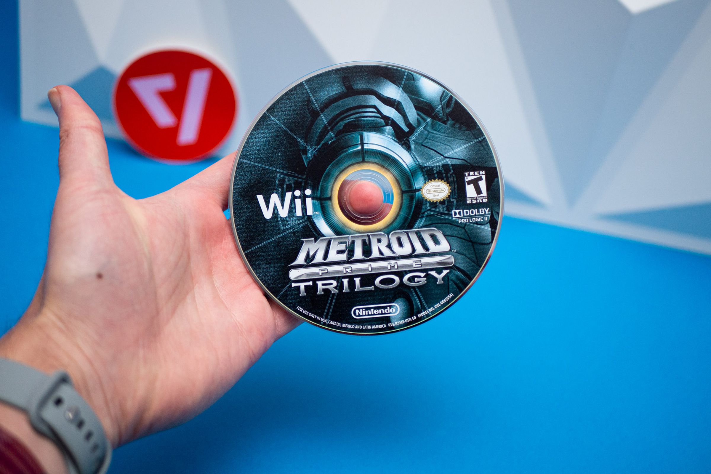Metroid Prime Trilogy को Nintendo Wii गेम डिस्क समातेको हातको तस्वीर।