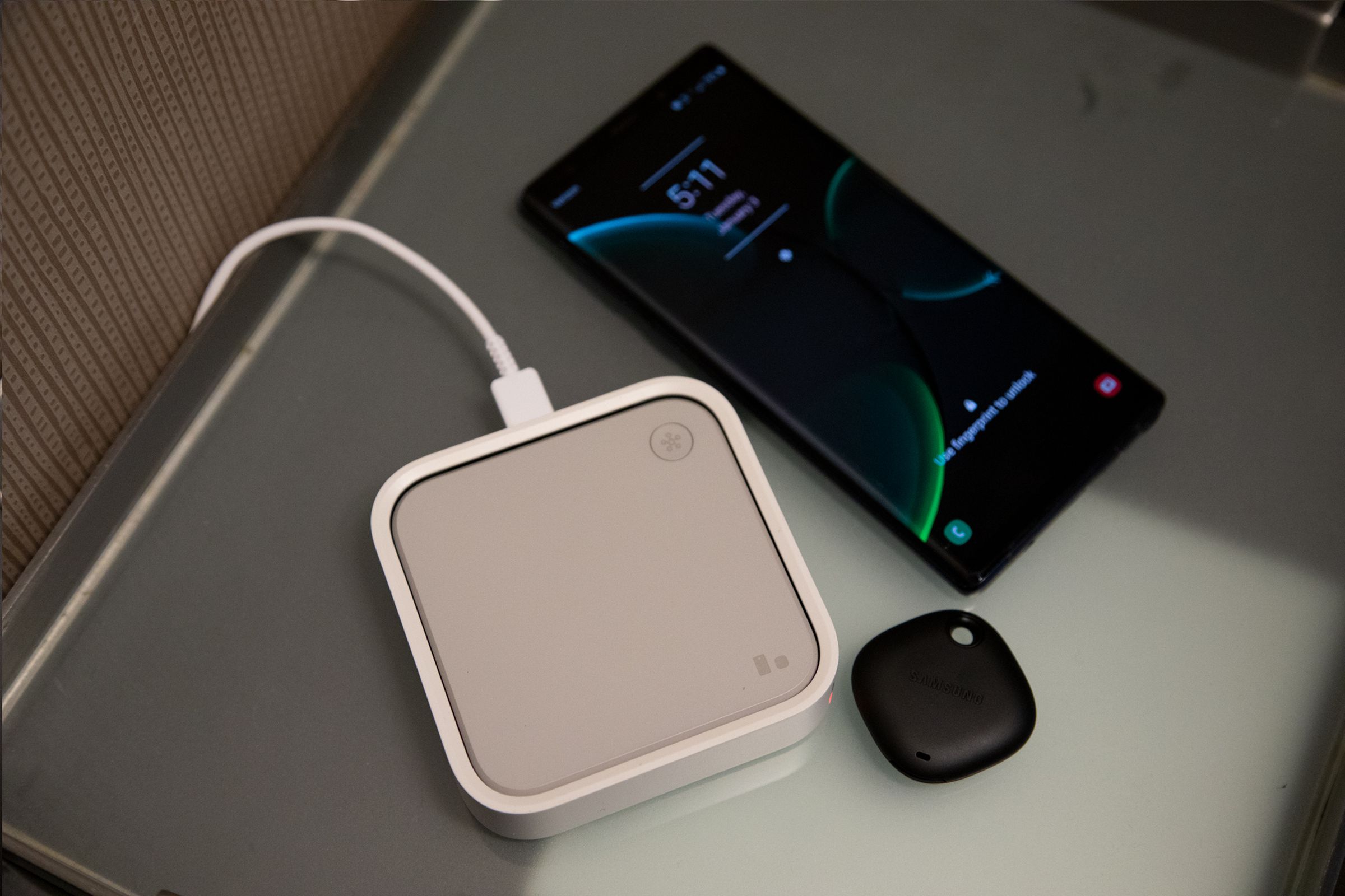 A grey and white wireless charging pad on a table next to a Galaxy phone and a black Galaxy tag.