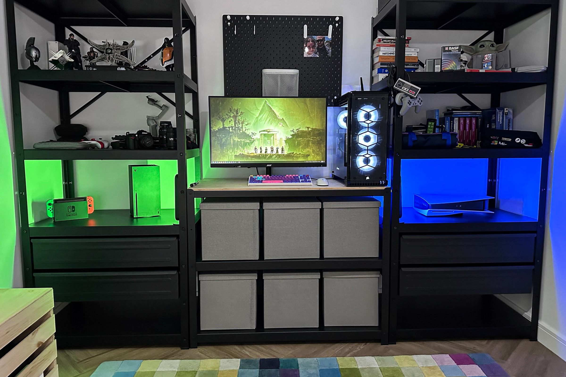 A tabletop with a monitor and PC; shelves on either side hold a variety of tech; the left shelf has a green light while the right shelf has a blue light.
