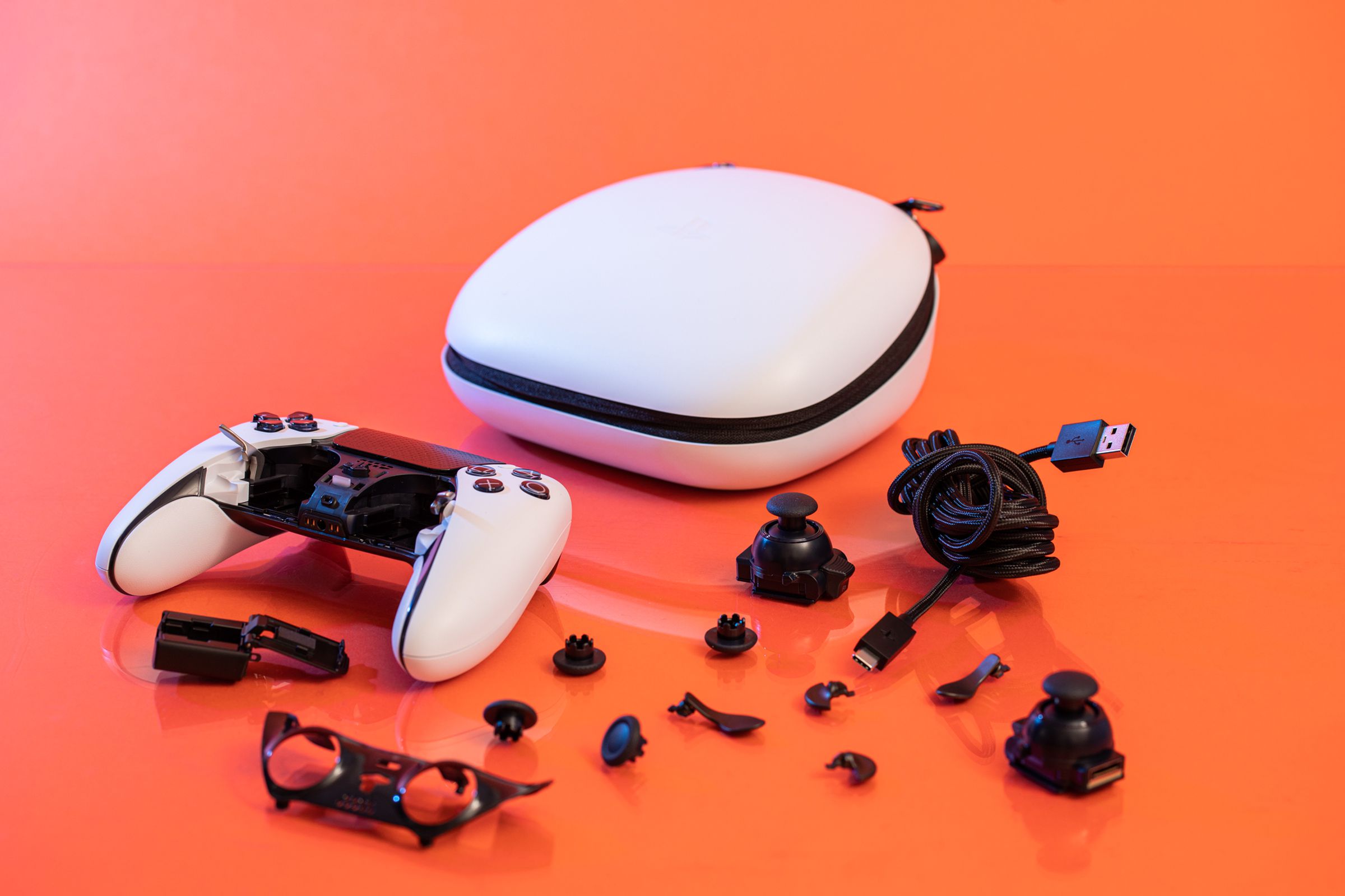 All of the accessories that are included with the DualSense Edge spread out on a table. It includes a cable, a hard case, four back paddles, four replaceable analog stick heads, and a cable locking mechanism.