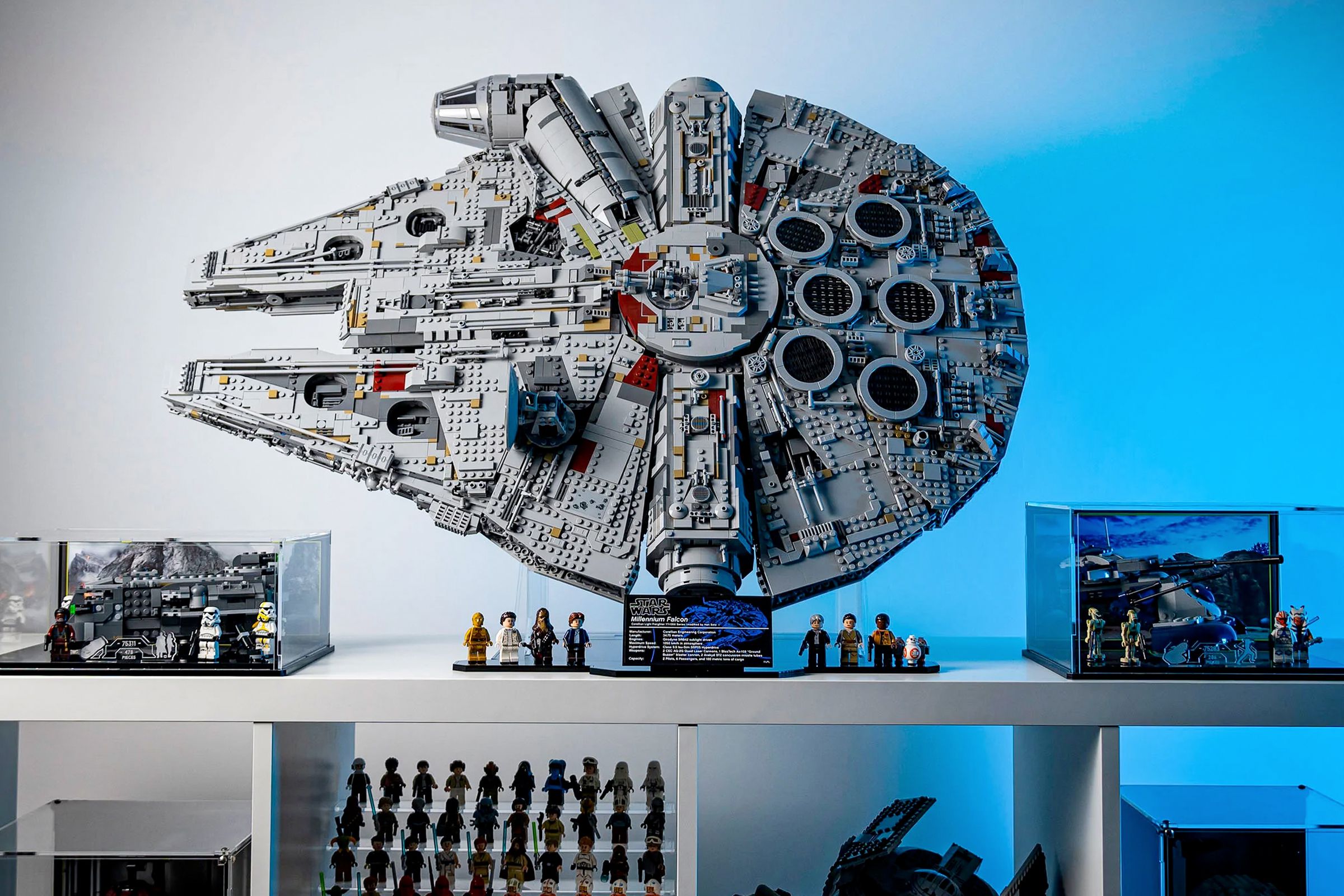 A built Lego Star Wars Millennium Falcon set mounted on a vertical stand from Wicked Brick, sitting atop a white shelf with other Star Wars collectibles.
