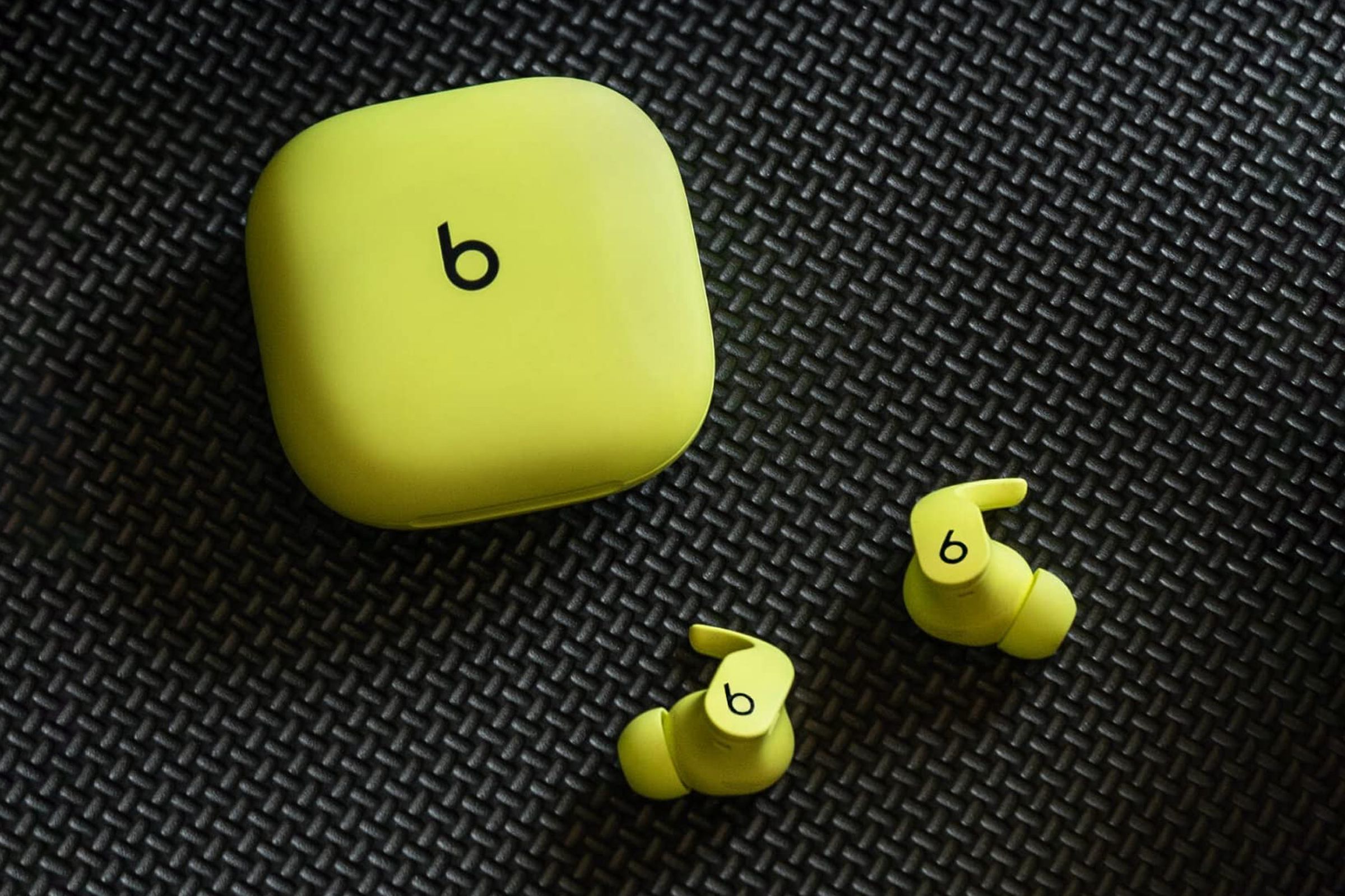 The bright yellow version of the Beats Fit Pro earbuds and their matching case resting on a black mesh pattern.