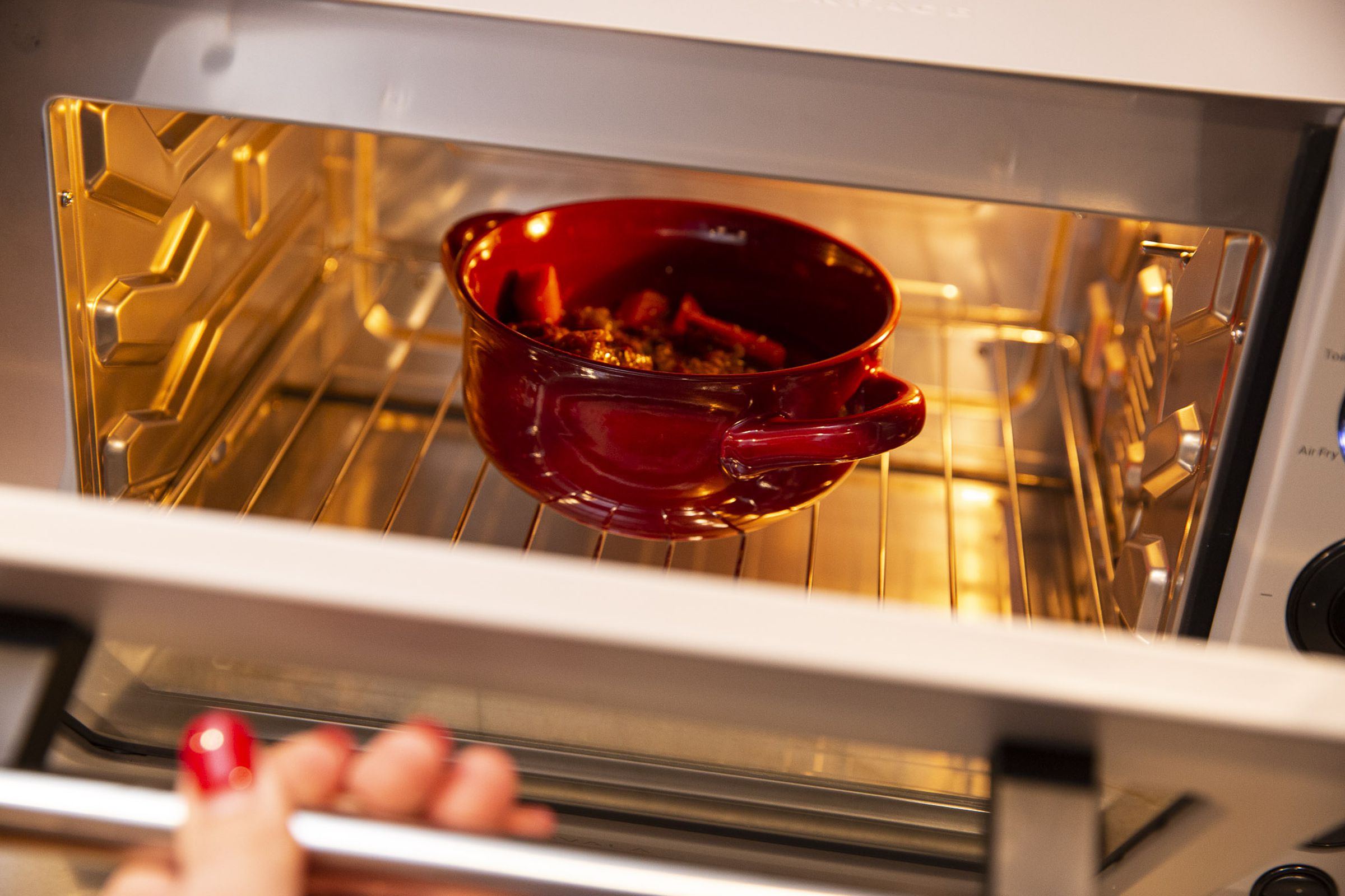 A red bowl in a small countertop oven with the door open.