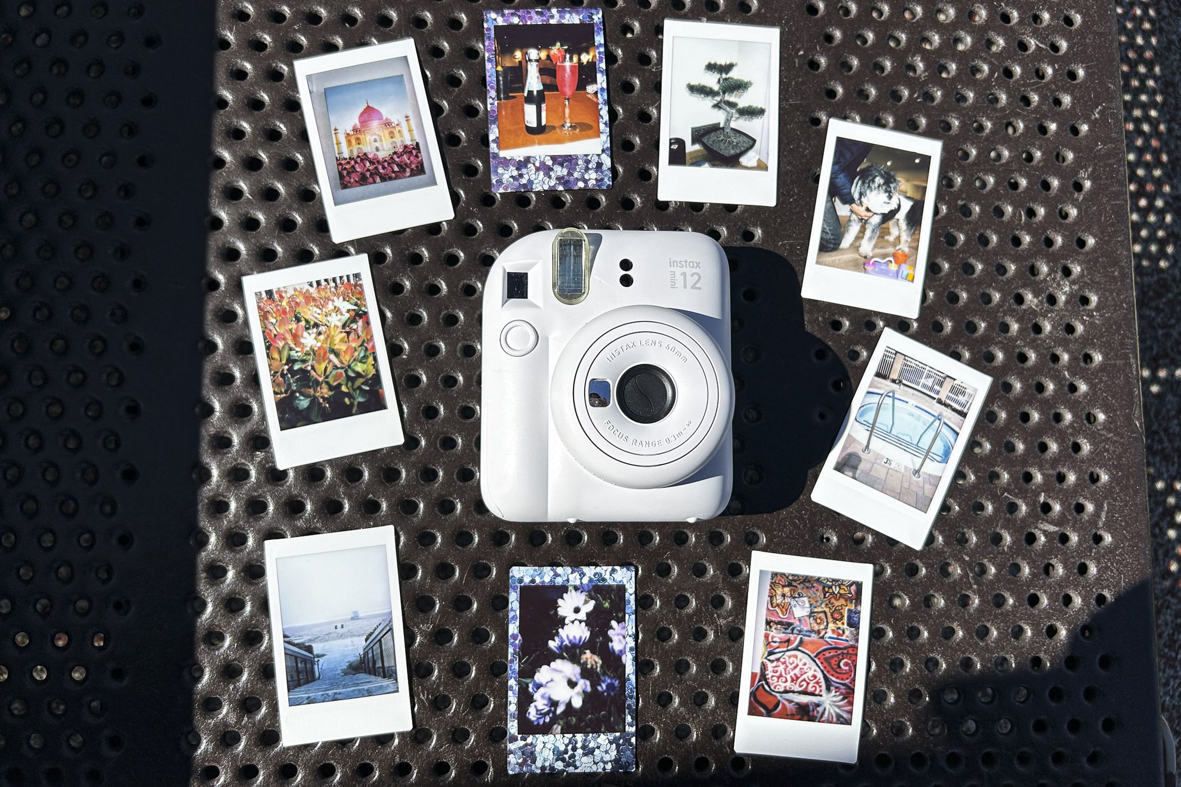 A white Fujifilm Instax Mini 12 instant camera surrounded by wallet-sized photos it produced.
