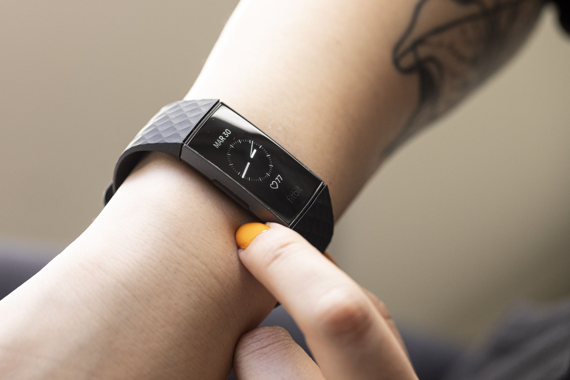 Side view of a person reaching to press the inductive button on the Fitbit Charge 3