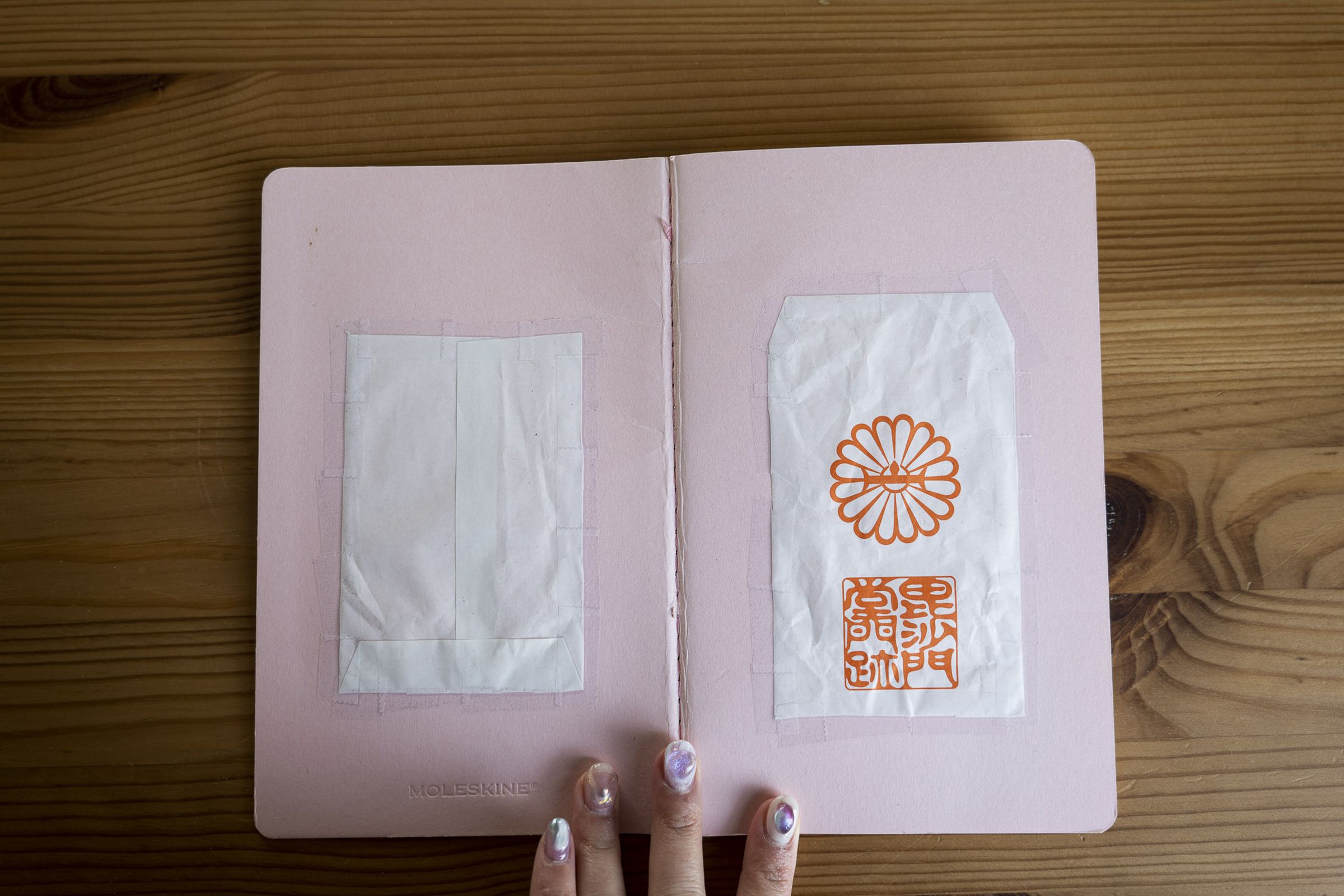 A Moleskine notebook opened with the cover facing up. A cut open paper envelope is taped onto the front and back cover of the notebook.