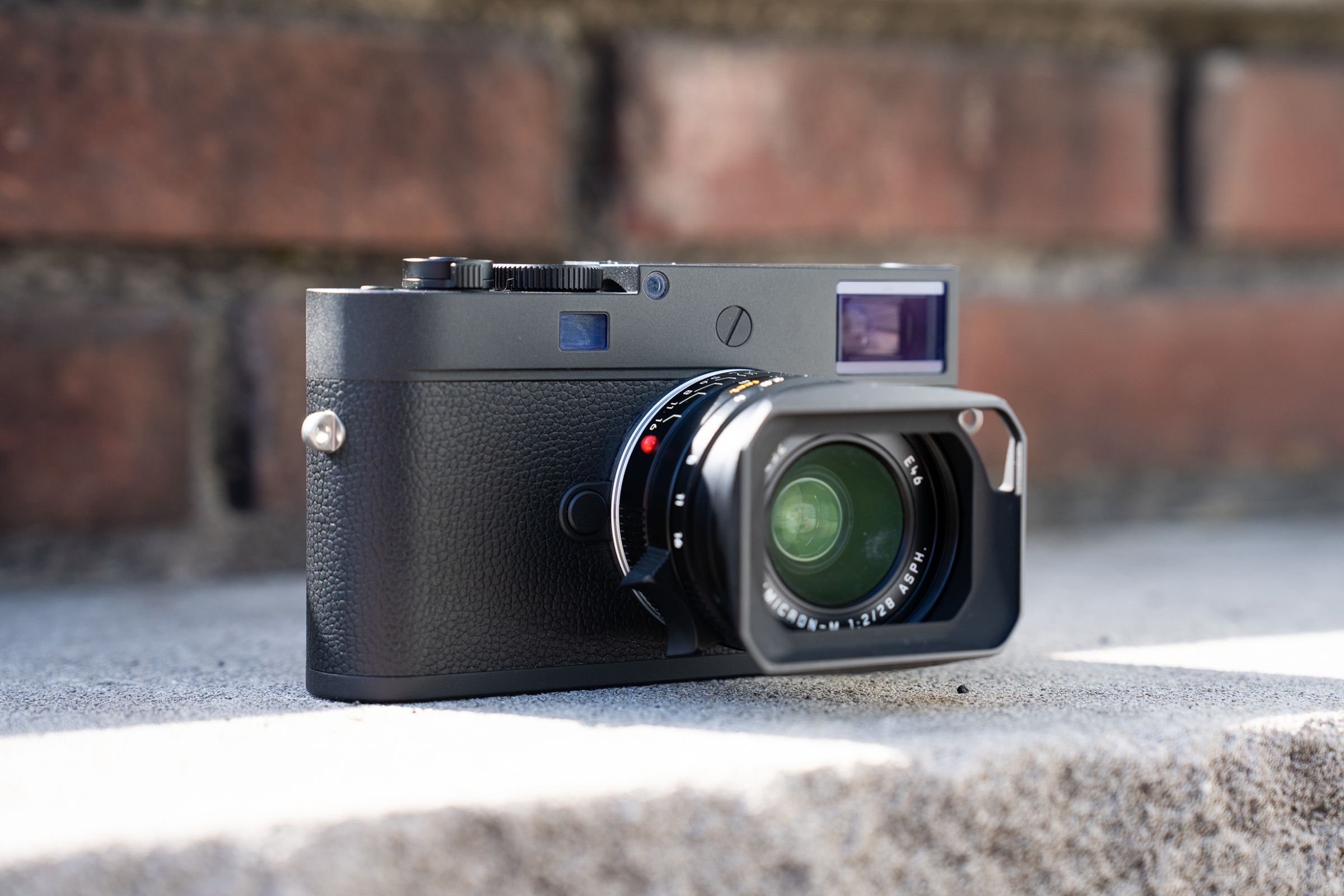 The M11 Monochrom digital rangefinder camera sitting on a stone ledge in front of a brick wall.