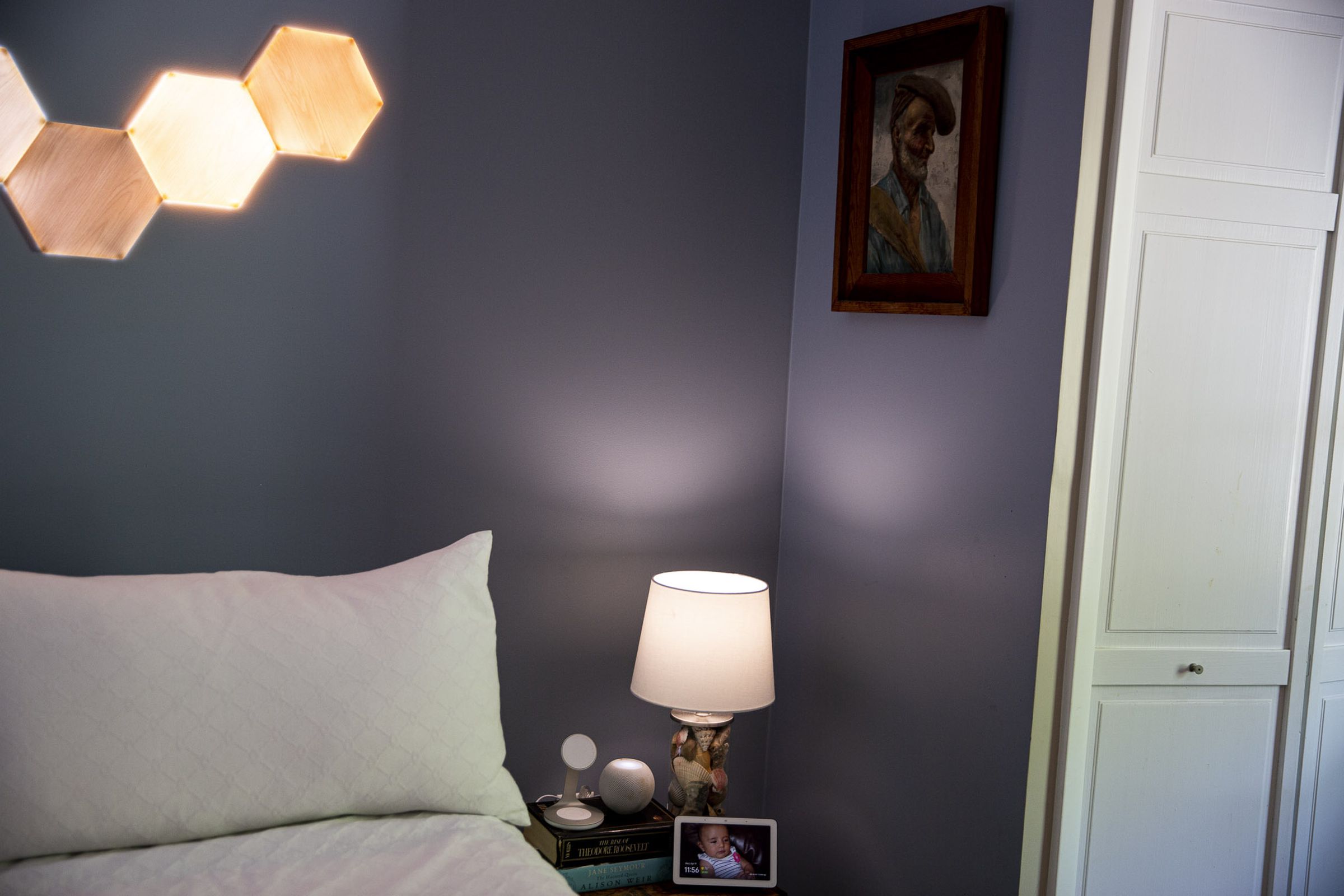 A lamp on a bedside table next to a bed with light panels on the wall behind it,