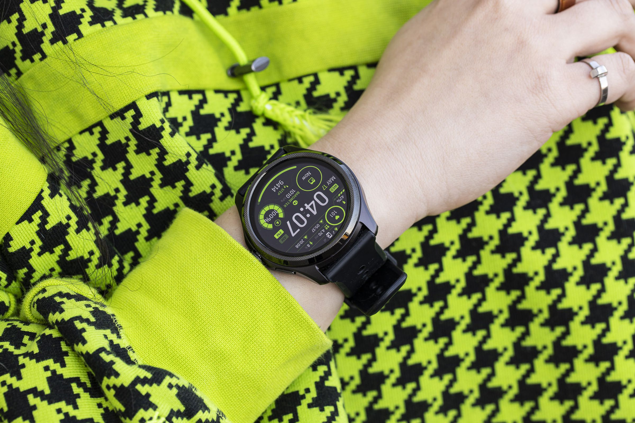 Close-up of the Mobvoi TicWatch Pro 5 on a wrist against a lime green / black sweater with a houndstooth pattern.