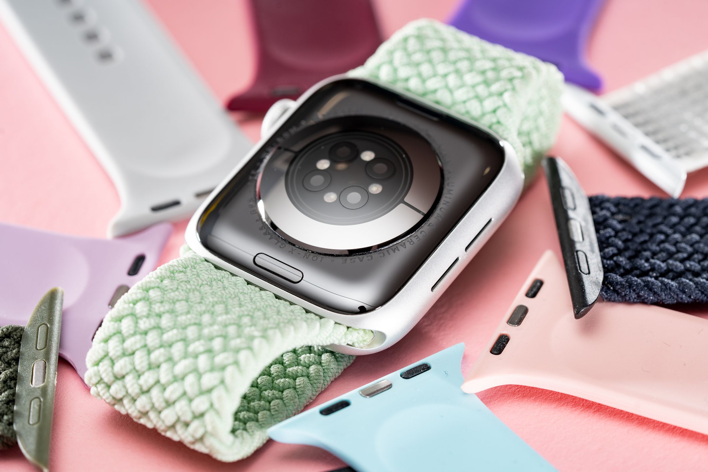 An upturned Apple Watch surrounded by spare straps, with its hidden band release button displayed prominently.