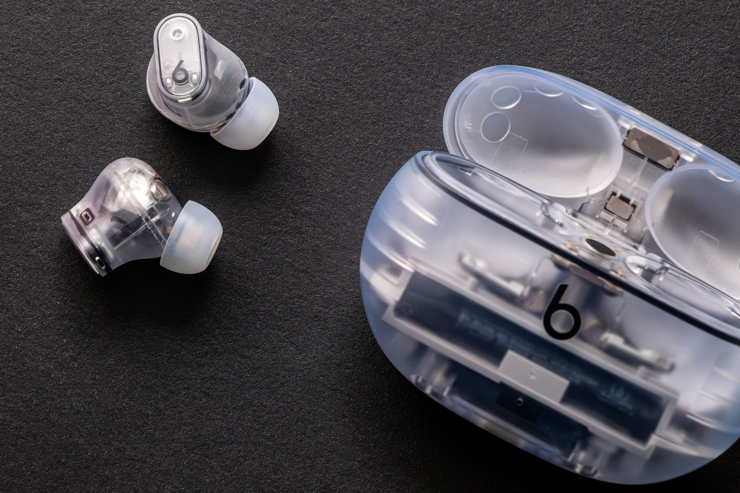 The see-through Beats Studio Buds Plus and their matching charging case, against a black background.