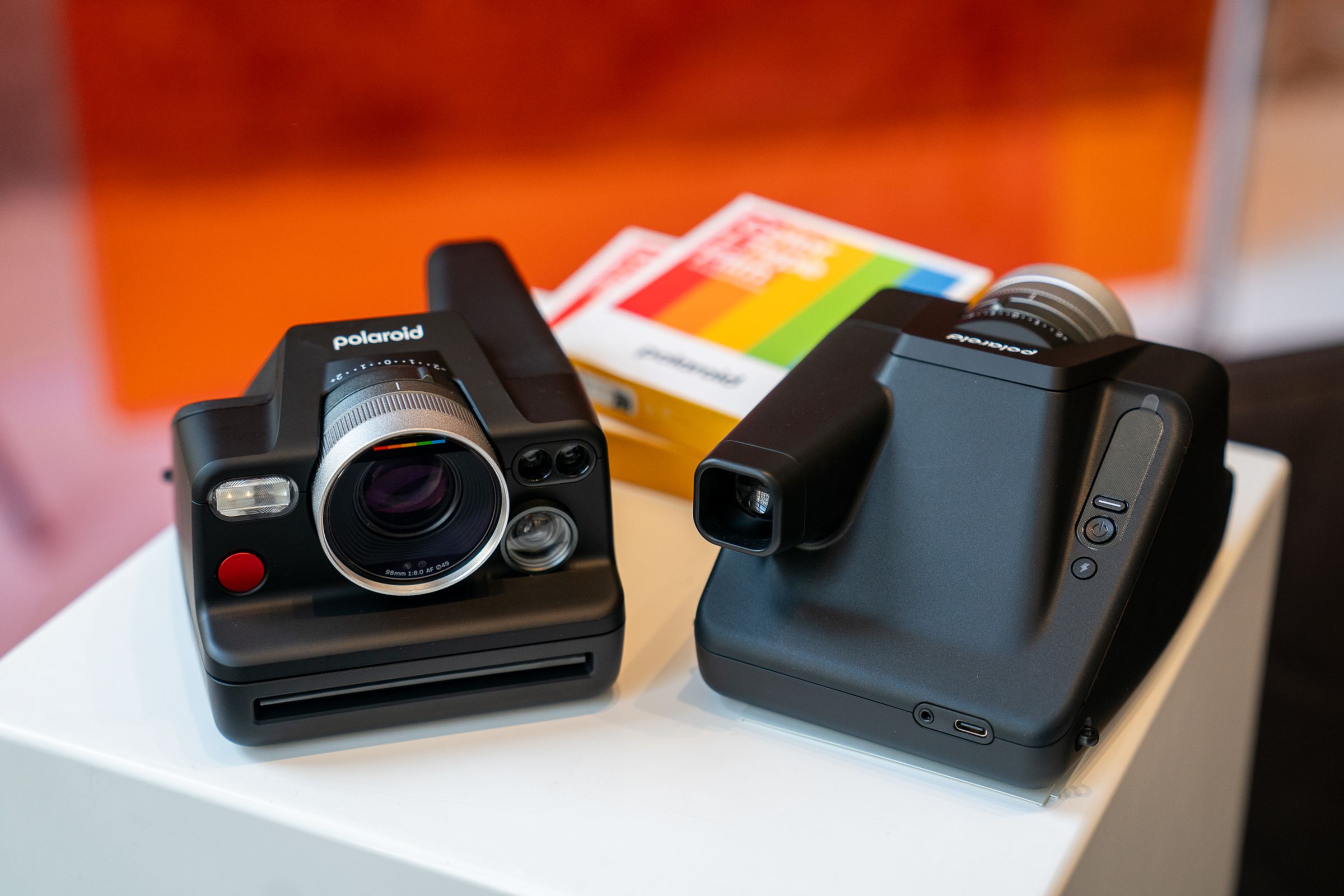 Two Polaroid I-2 instant cameras sitting on top of a counter. One shows the front while the other displays the back. A pack of Polaroid film sits nearby.
