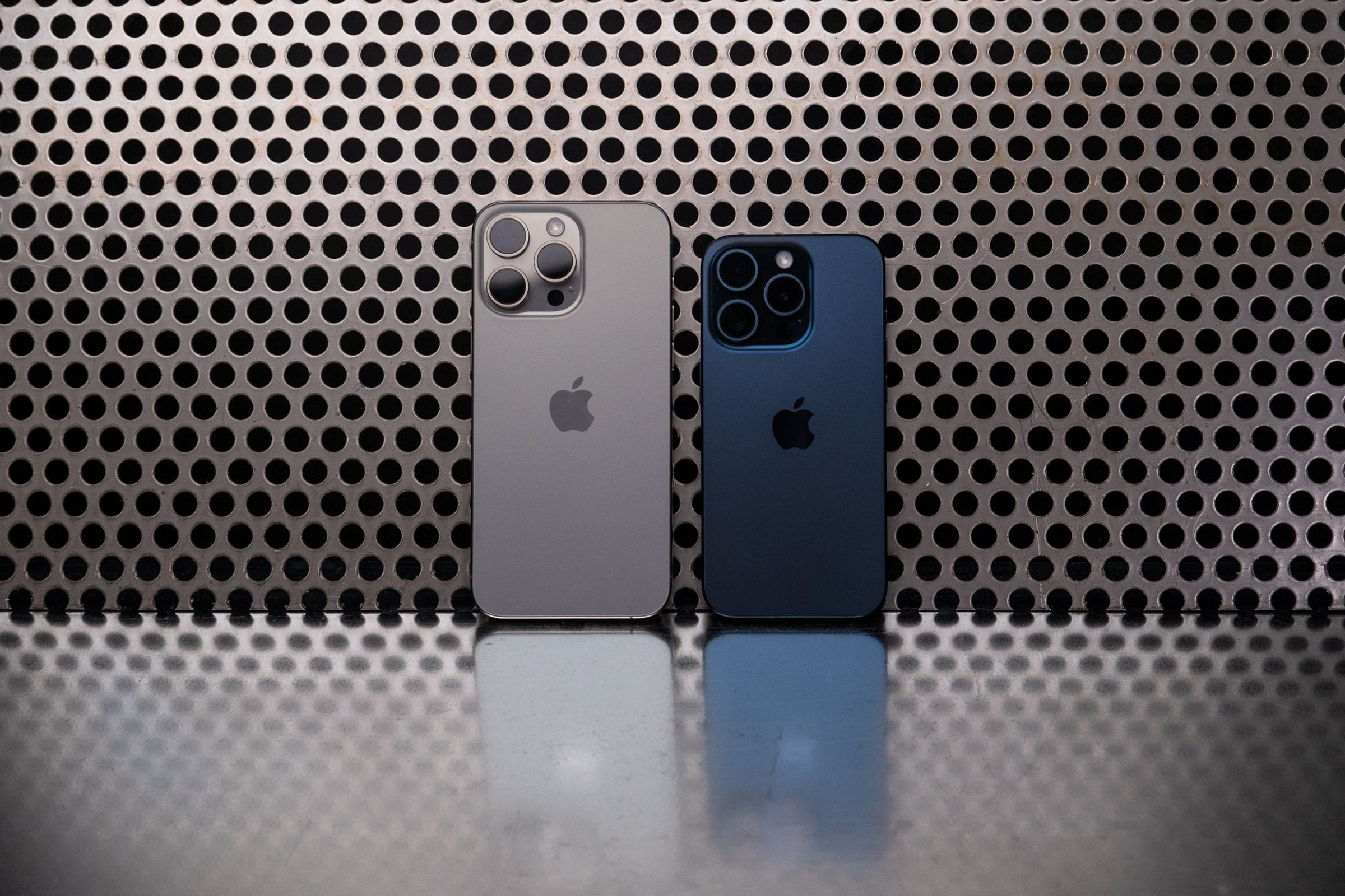 Photo of iPhone 15 Pro and Pro Max leaning against a metal background.