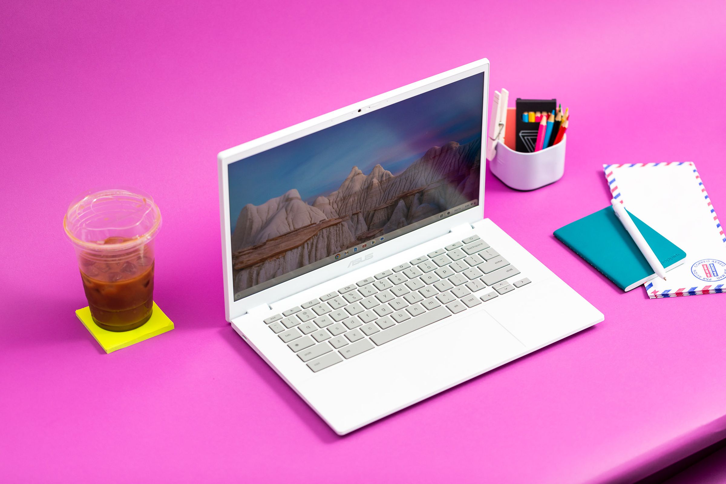 The Asus Chromebook Plus CX34 on a pink table with a coffee and post-it pad beside it.