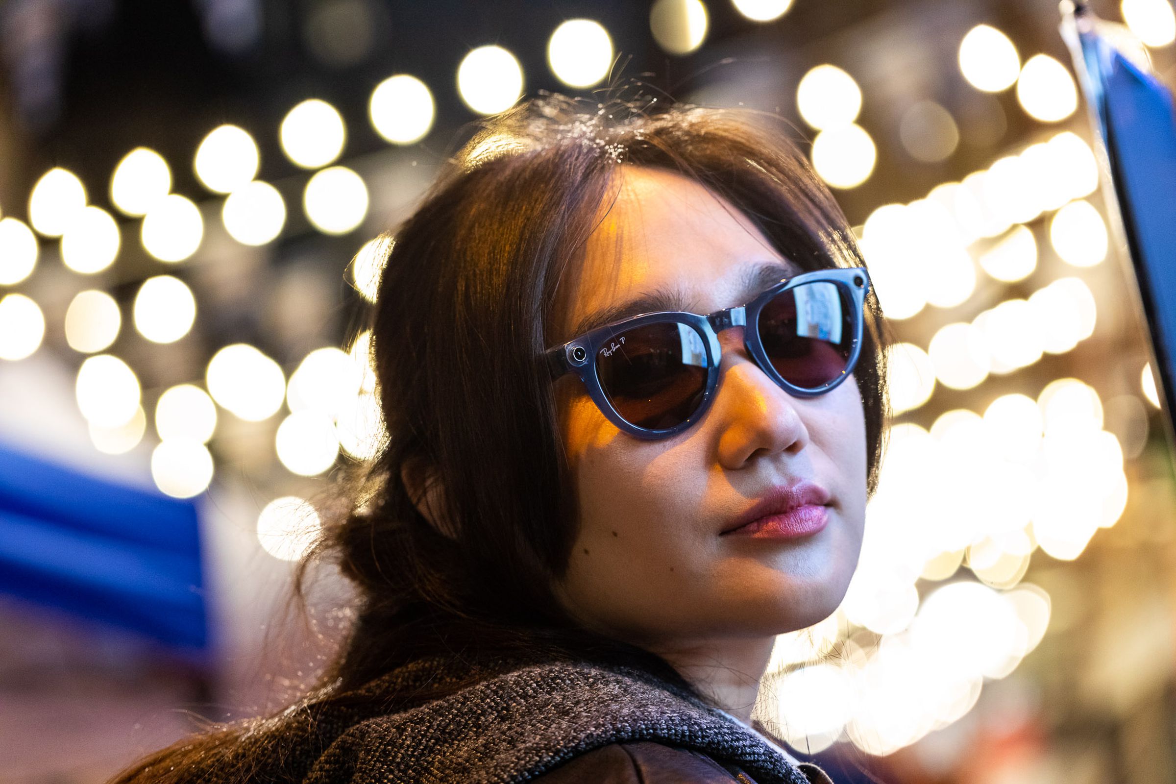 Person wearing Ray-Ban Meta smart glasses with string lights in the background.