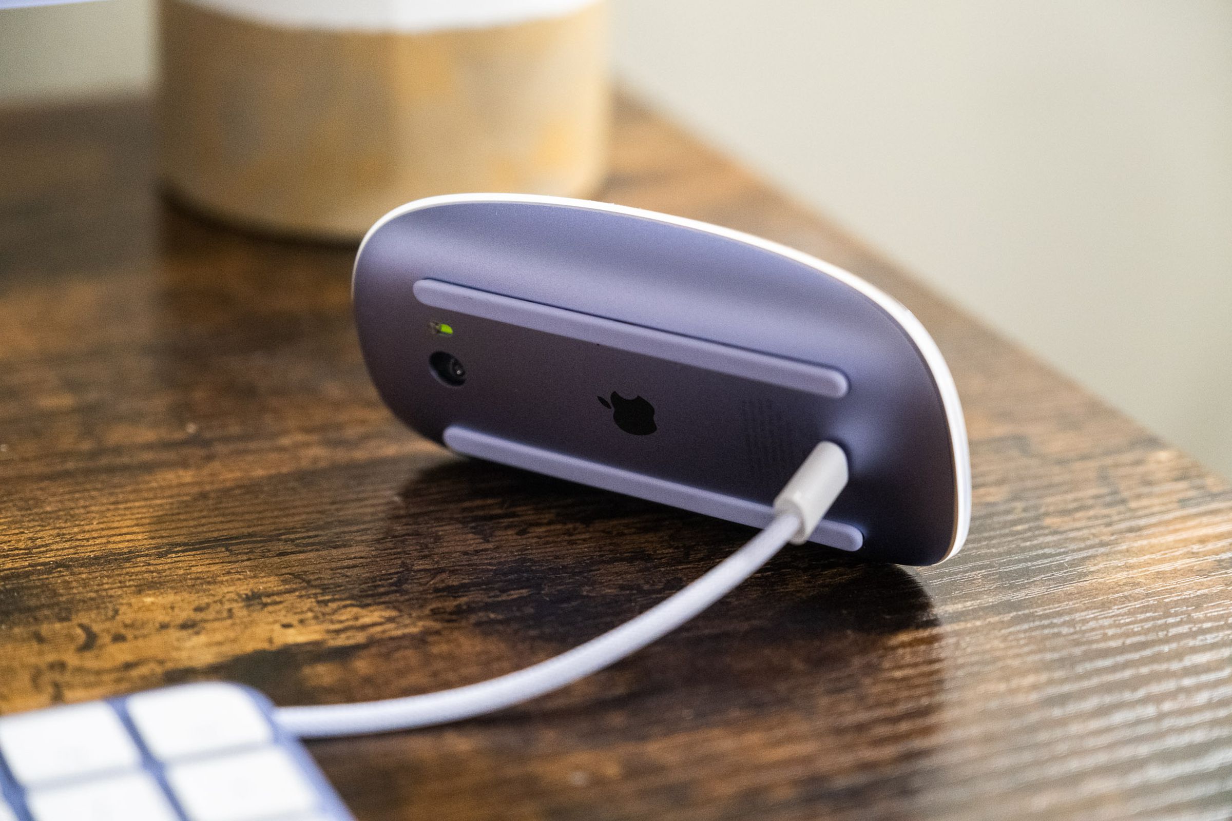 A purple Apple Magic Mouse charging via its Lightning port on the under side
