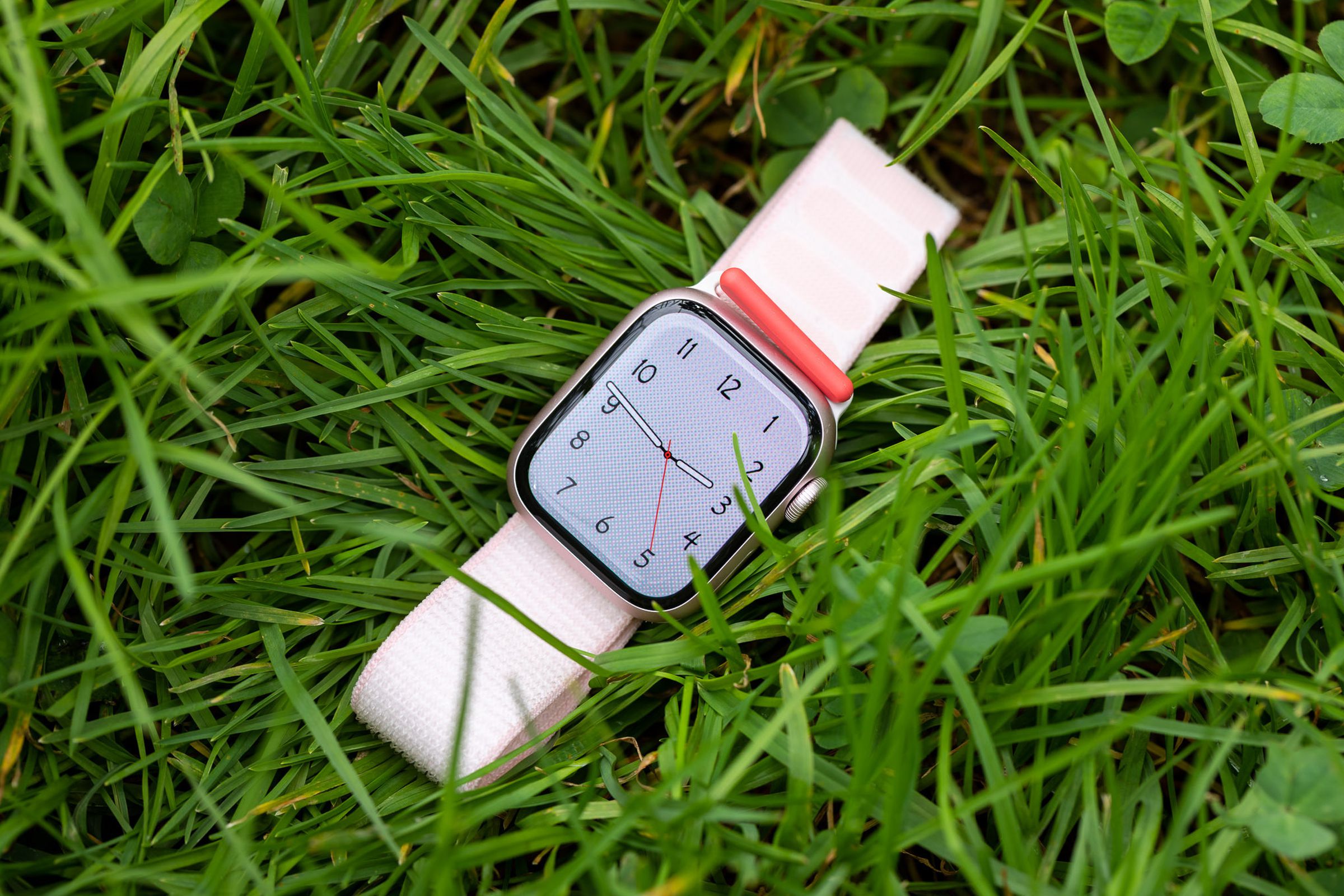 The pink Apple Watch Series 9 lying on grass.