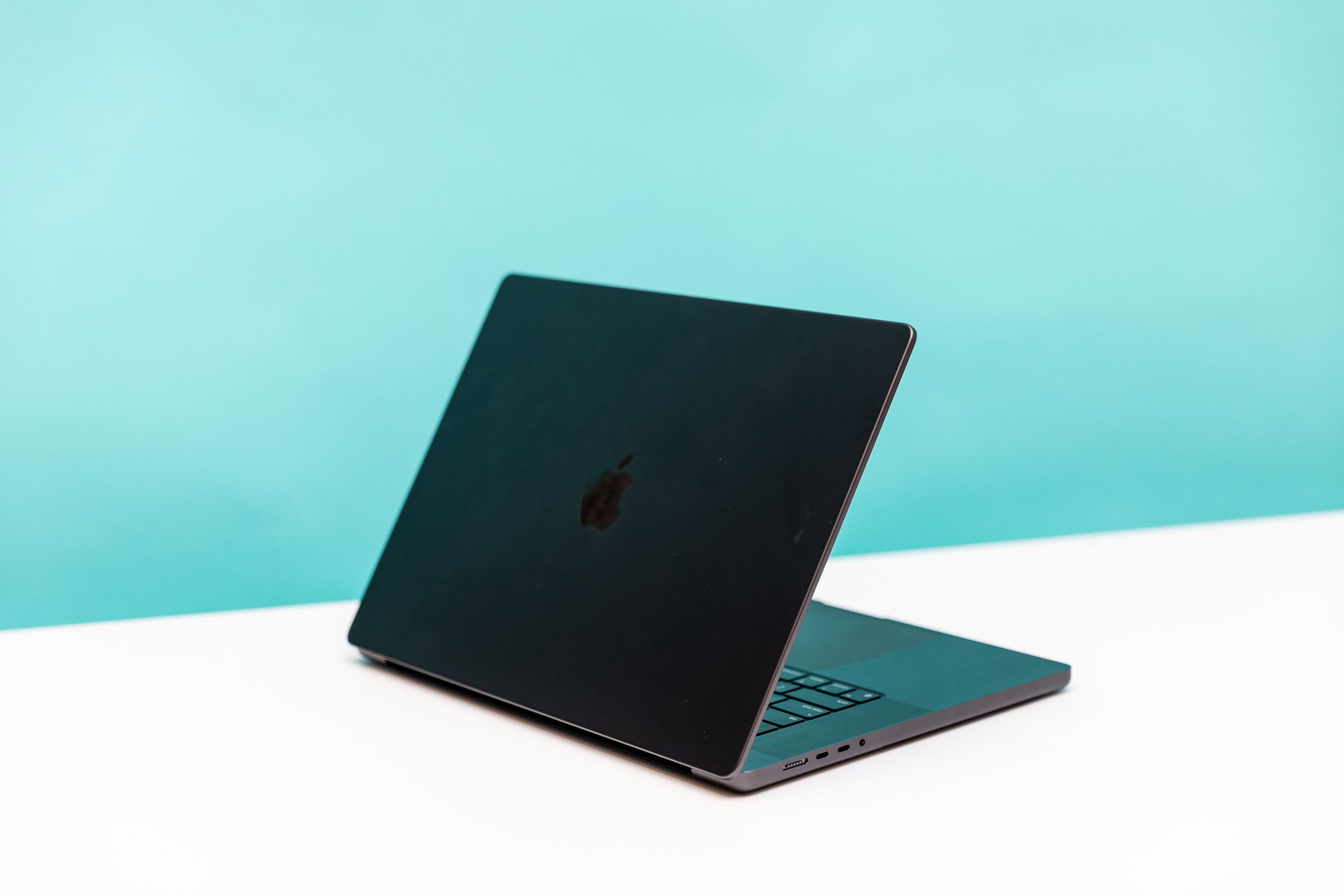 Angled side view of a MacBook Pro 16 with M3 Max in front of a teal and white background.