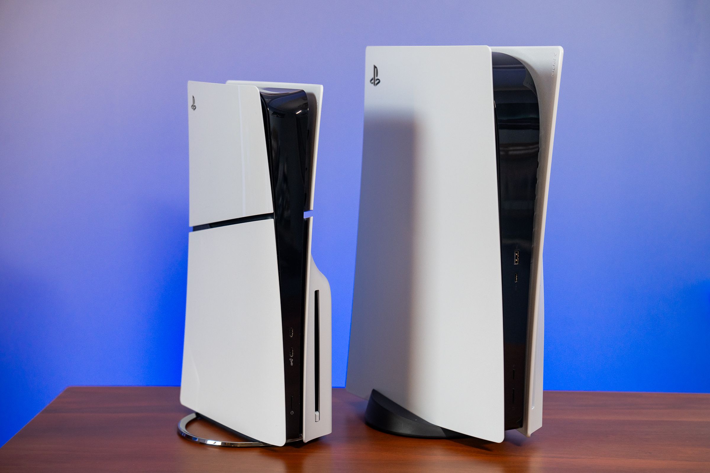 The new PlayStation 5 slim and standard PlayStation 5 standing vertically side by side on a table.
