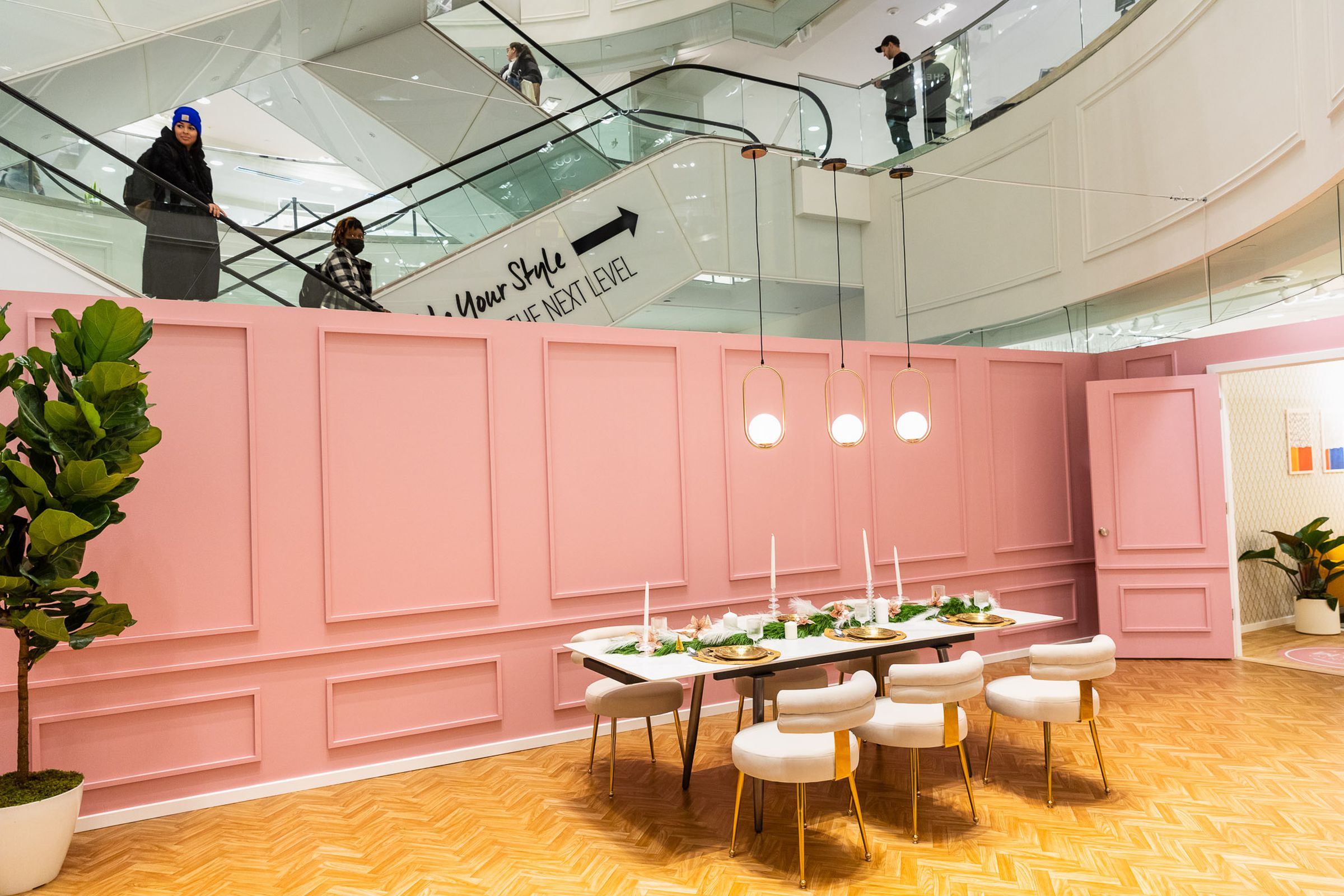 A pink walled room sits in the basement level of Forever 21. Right above where the wall ends, a woman is descending the escalator, looking into the pop-up space.