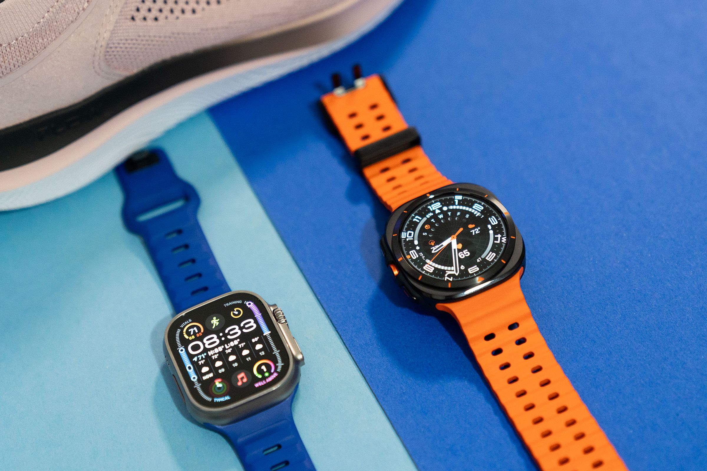 Apple Watch Ultra 2 next to the Samsung Galaxy Watch Ultra with a pink sneaker in the background