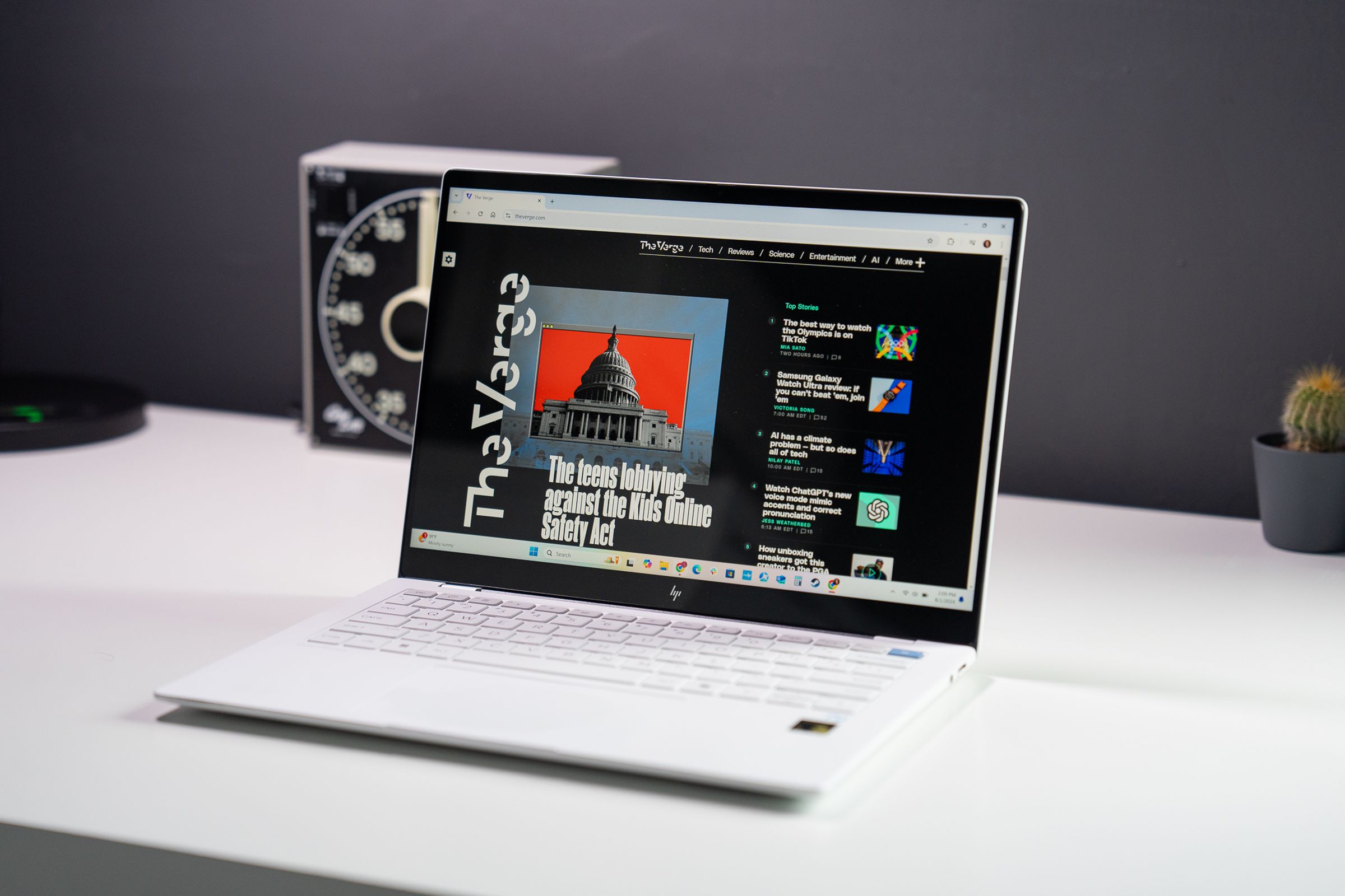 An open and powered on white laptop sits on top of a white surface against a dark gray background.