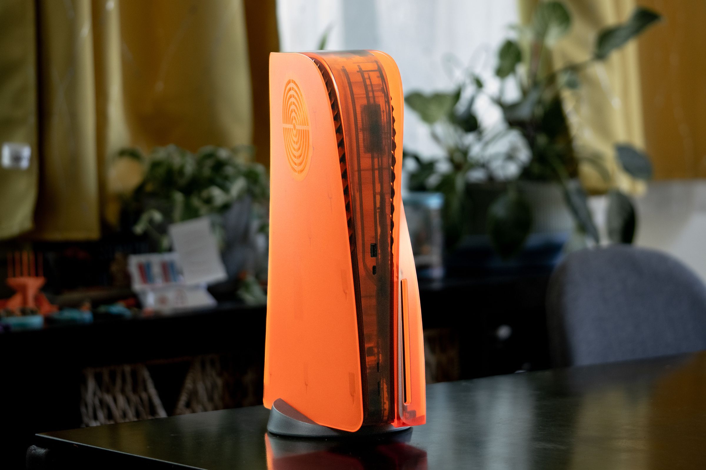 A Sony PlayStation 5 game console stands upright with translucent orange sides and an orange skin running up and down its center bar.