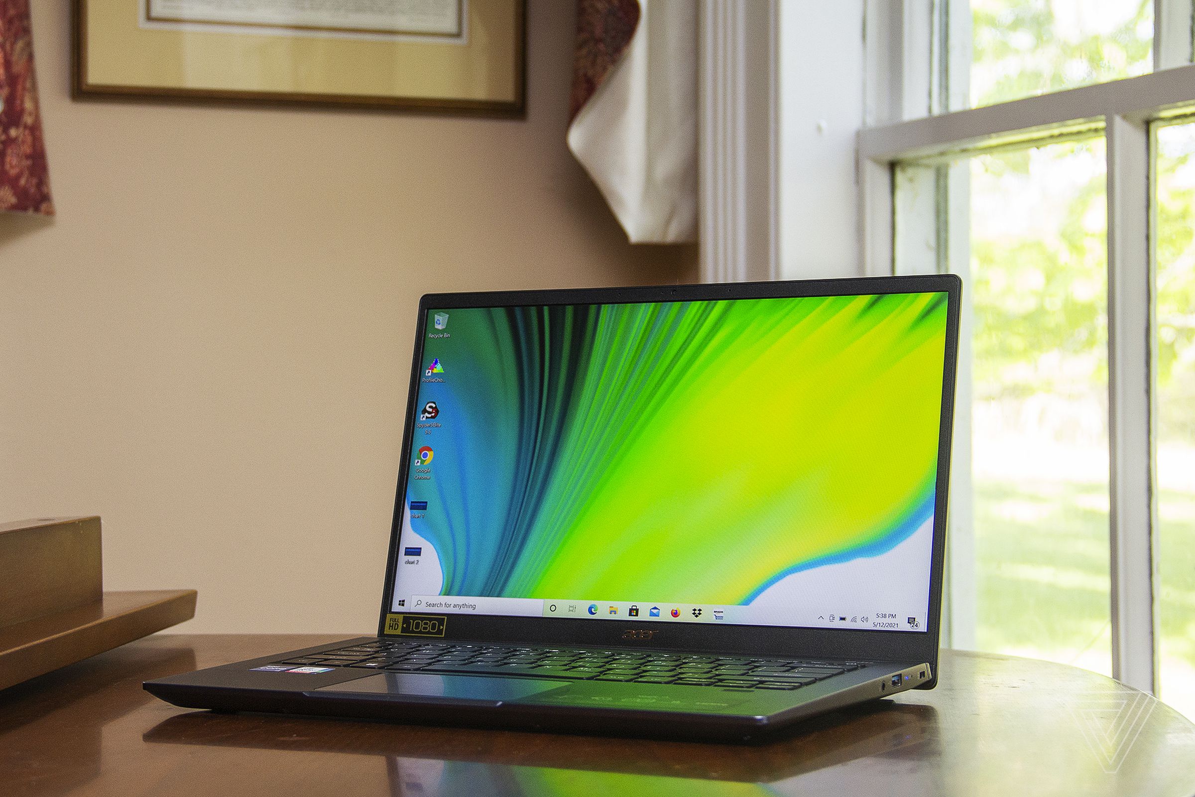 The Acer Swift 3X open on a piano, angled to the left. The screen displays a blue, green, and white gradient.