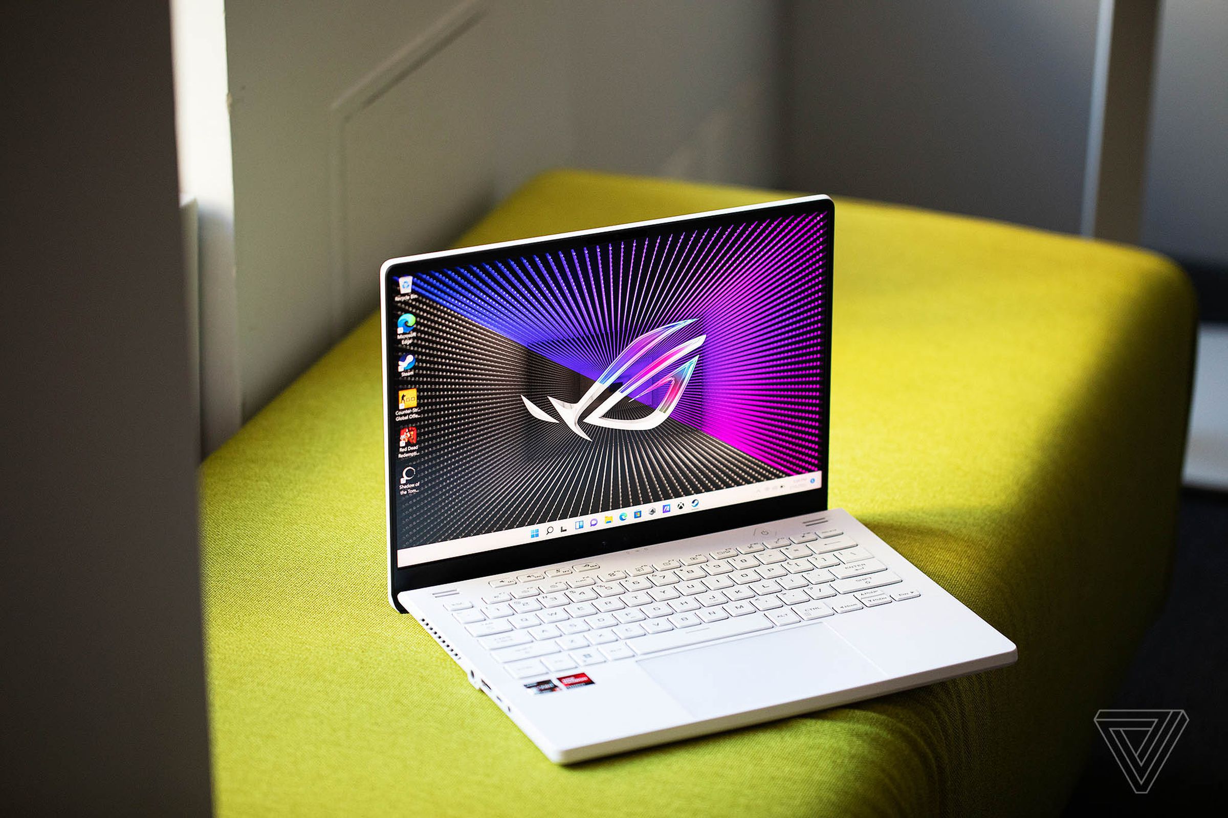 The Asus ROG Zephyrus G14 on a green bench open angled slightly to the right. The screen displays a black and purple background with the ROG logo.