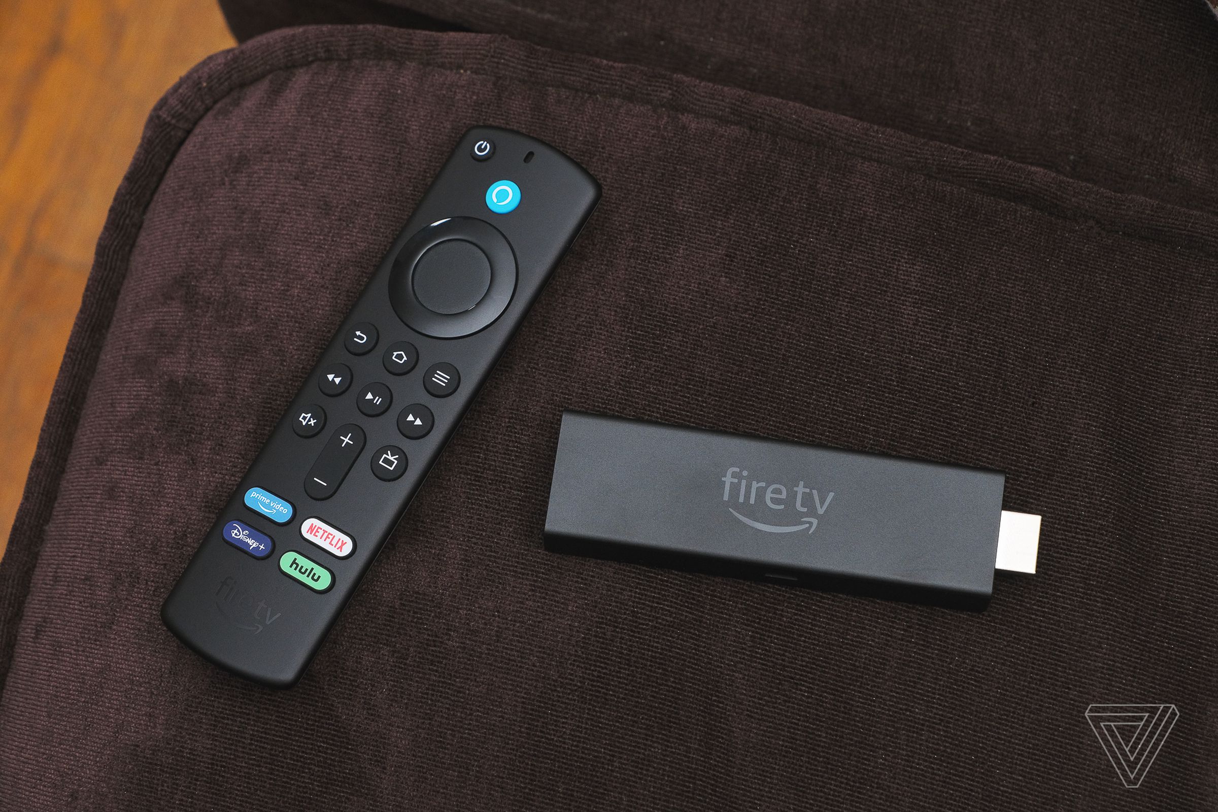 A close-up of the Amazon Fire TV Stick 4K Max streaming dongle beside its remote control on a brown couch.