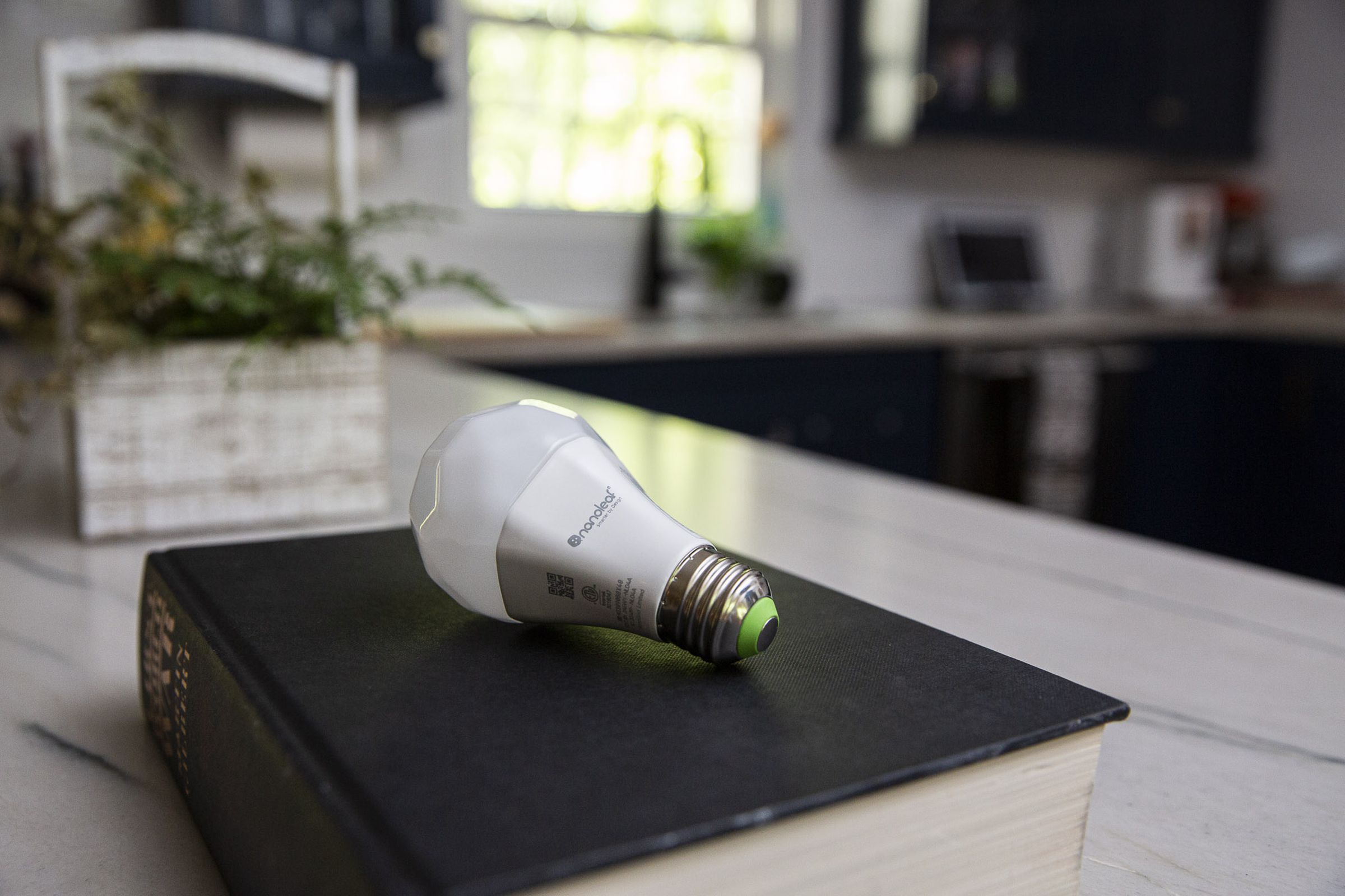 A Nanoleaf Essentials Matter A19 light bulb on a black book on a kitchen counter.