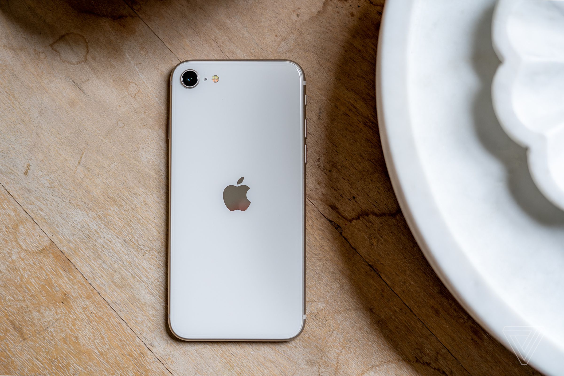 Photo of an iPhone SE 2022 laying on a wooden table next to some plates.