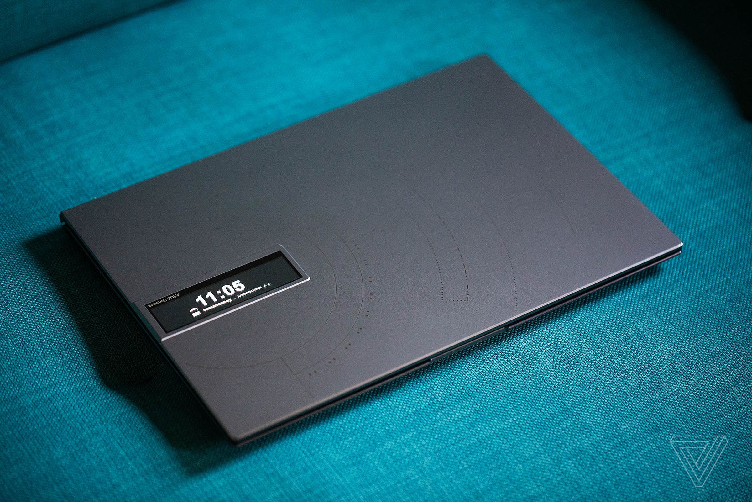 The Asus Zen book 14 OLED Space Edition closed, seen from above, on a green couch.