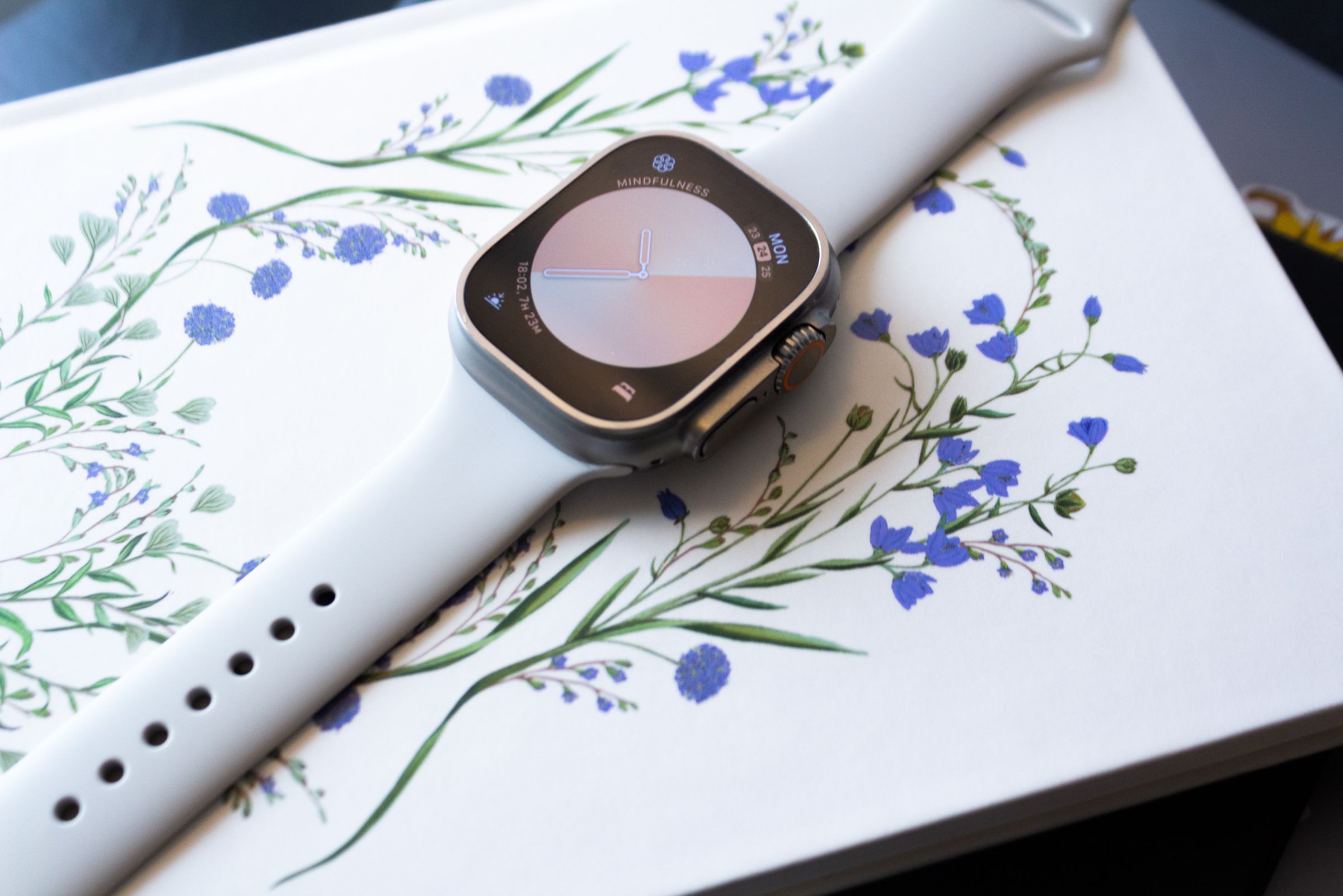 The Apple Watch Ultra with the 45mm Sport Band in Starlight on top of a book