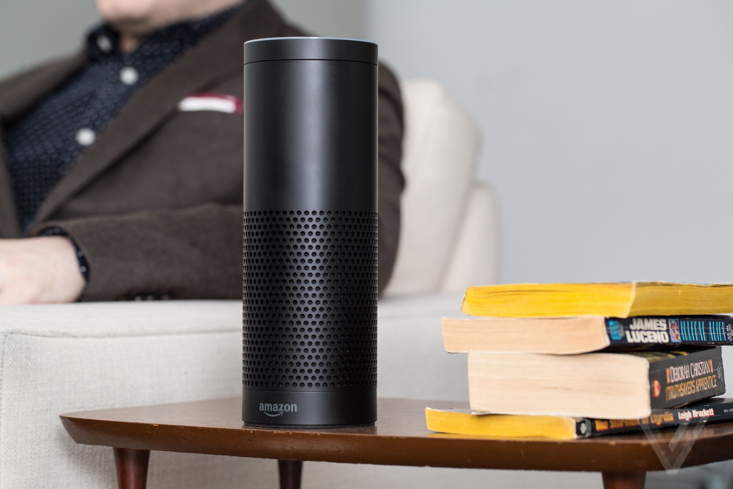 A 1st-gen Amazon Echo on a table besides a couch.