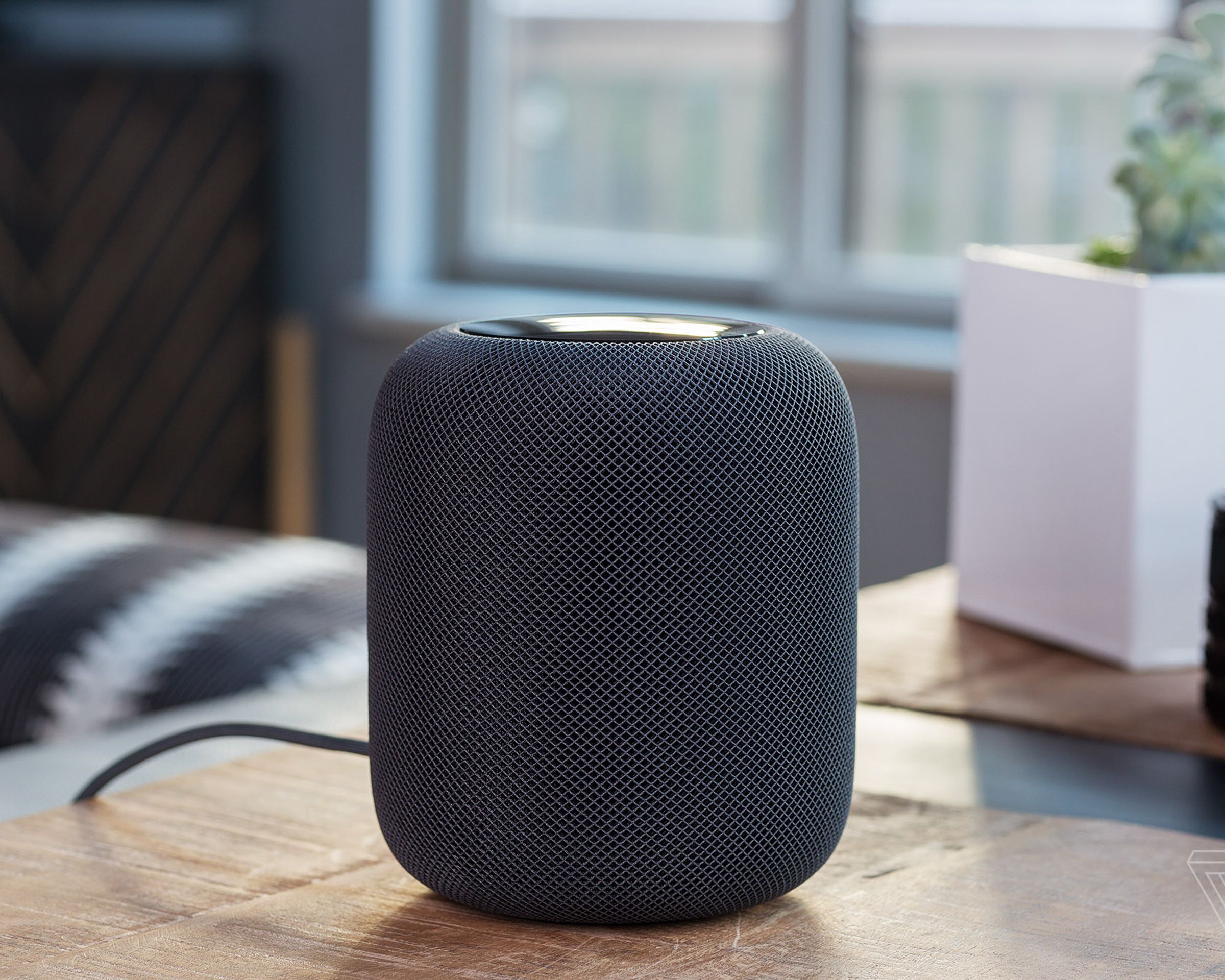 A first-generation HomePod on a desk in a room.