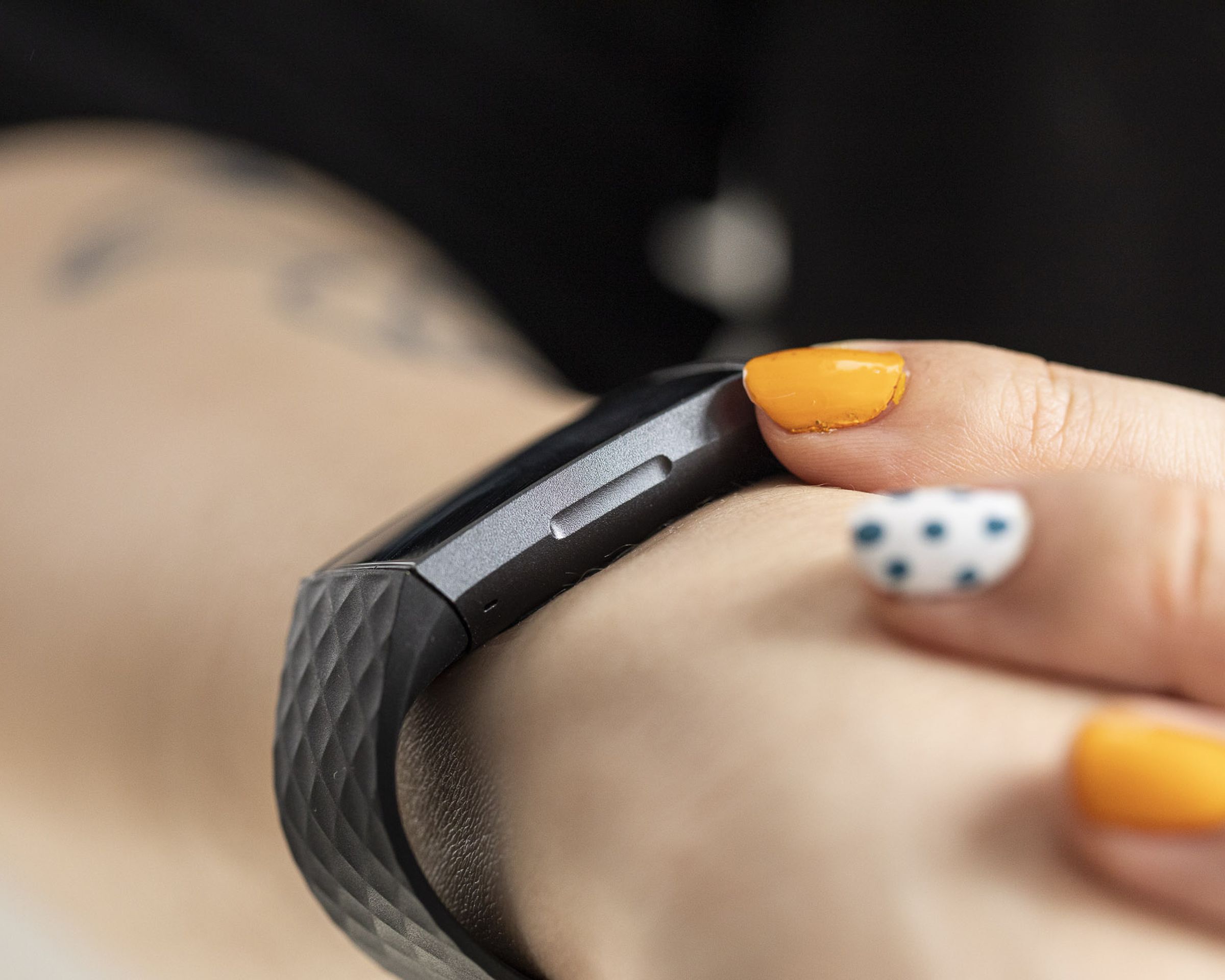 Person with colorful manicure using the Fitbit Charge 3 with a clear view of the inductive button.